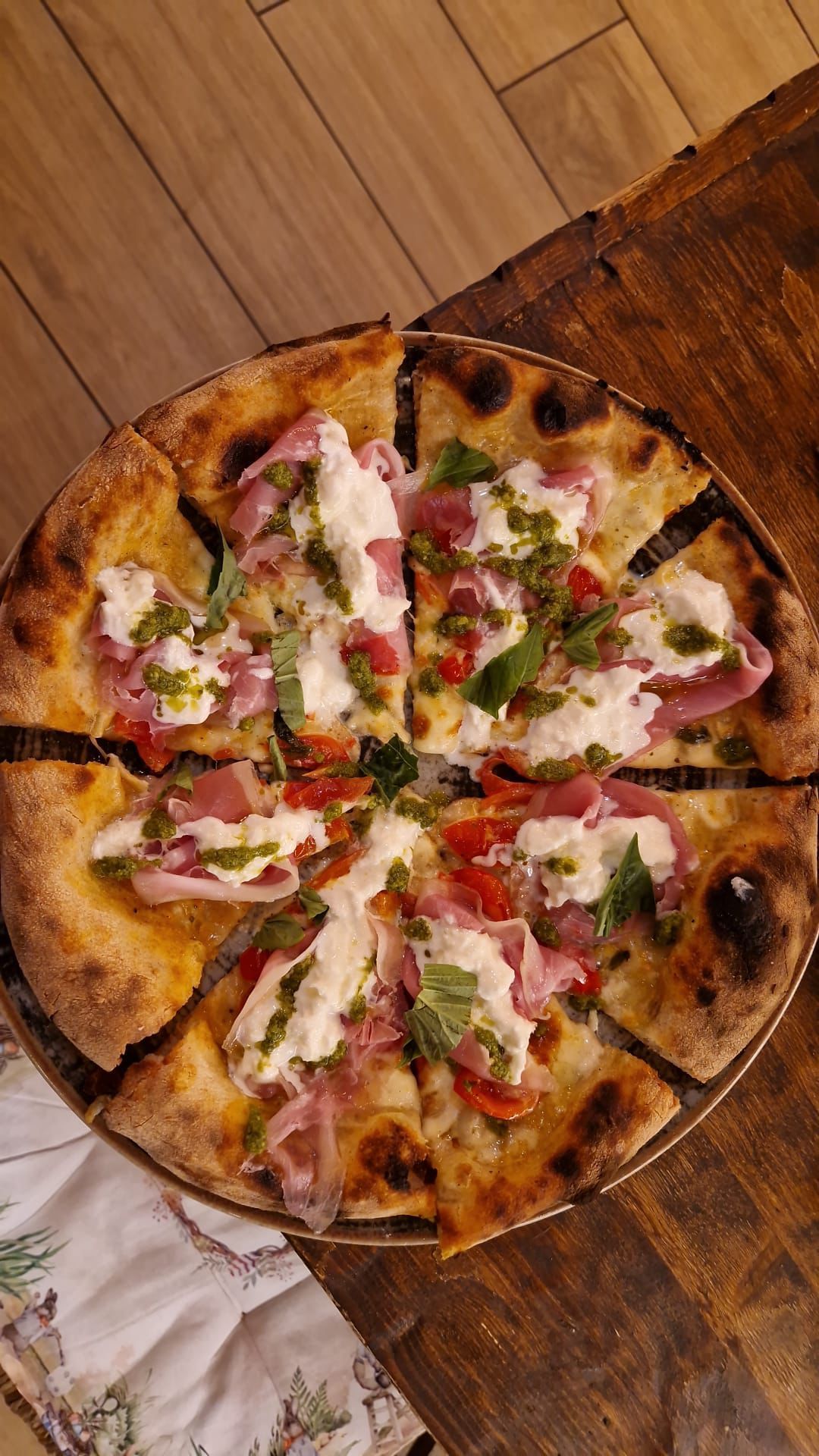 Pizza con burrata, prosciutto, basilico e pesto, tagliata a fette su una superficie di legno.