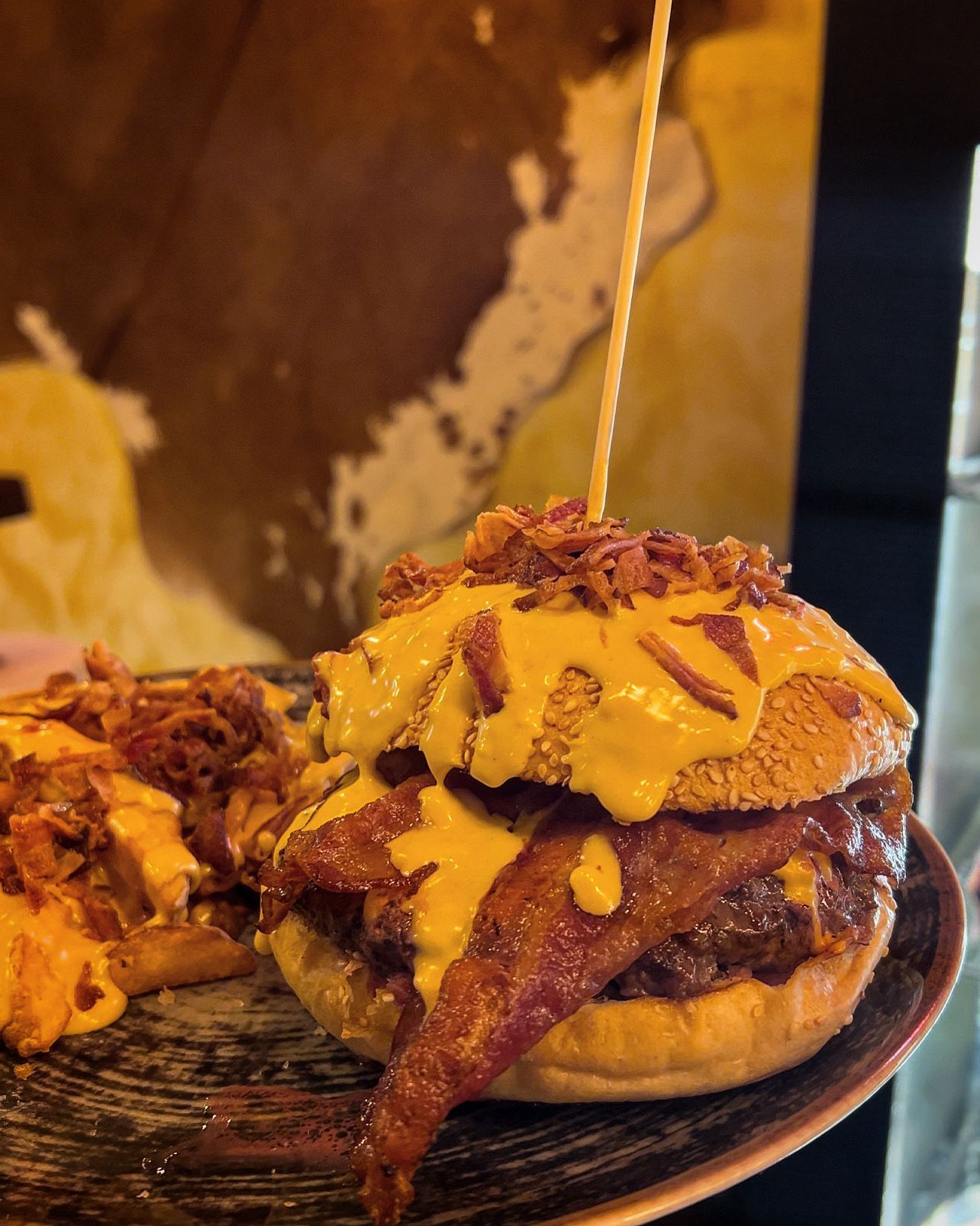 Cheeseburger con pancetta e salsa al formaggio, infilzato su un piatto, con patatine fritte a sinistra.