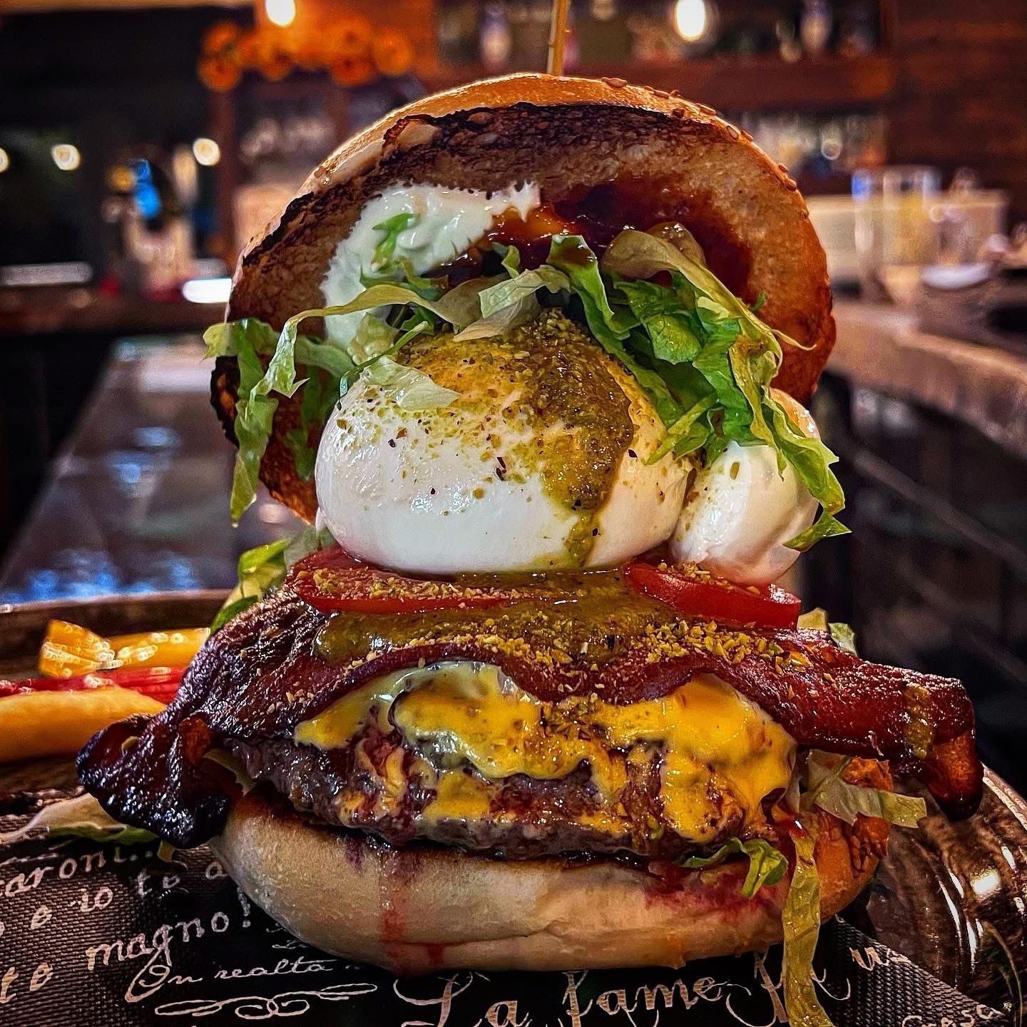 Hamburger con una grande palla di formaggio bianco, pancetta e salsa verde su un panino, su un piatto.