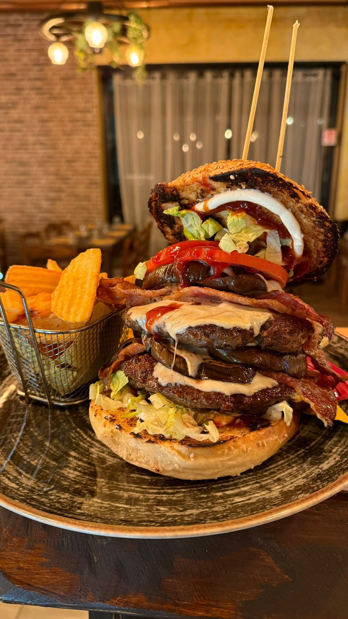 Hamburger impilato con patatine fritte su un piatto, in un ambiente da ristorante.