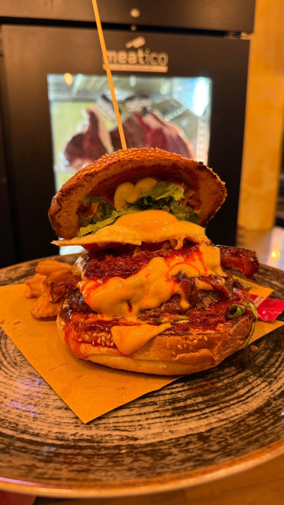 Hamburger con panino al sesamo, formaggio, salsa e contorni su un piatto.