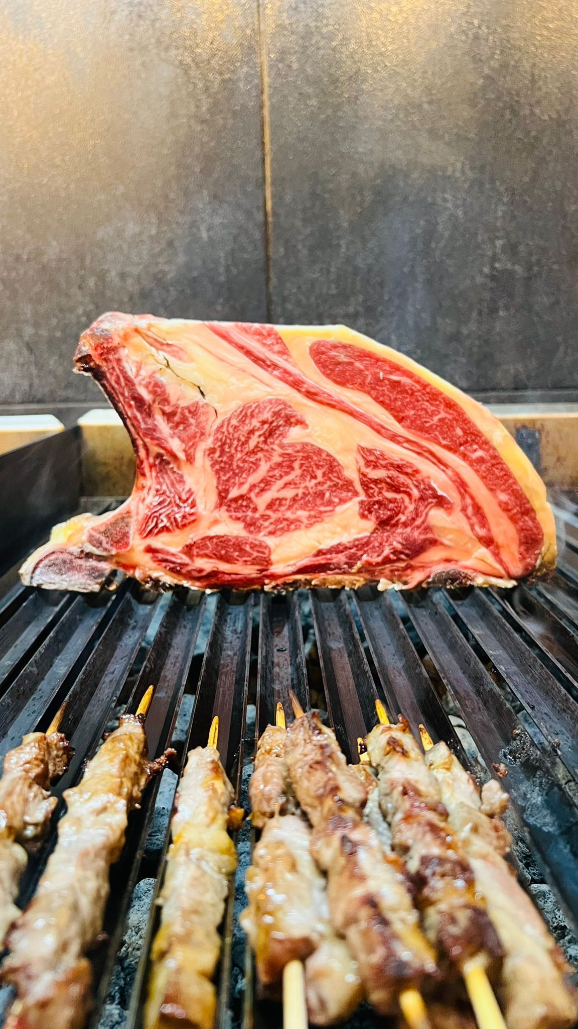 Grande bistecca di ribeye cruda su una griglia sopra spiedini di carne.