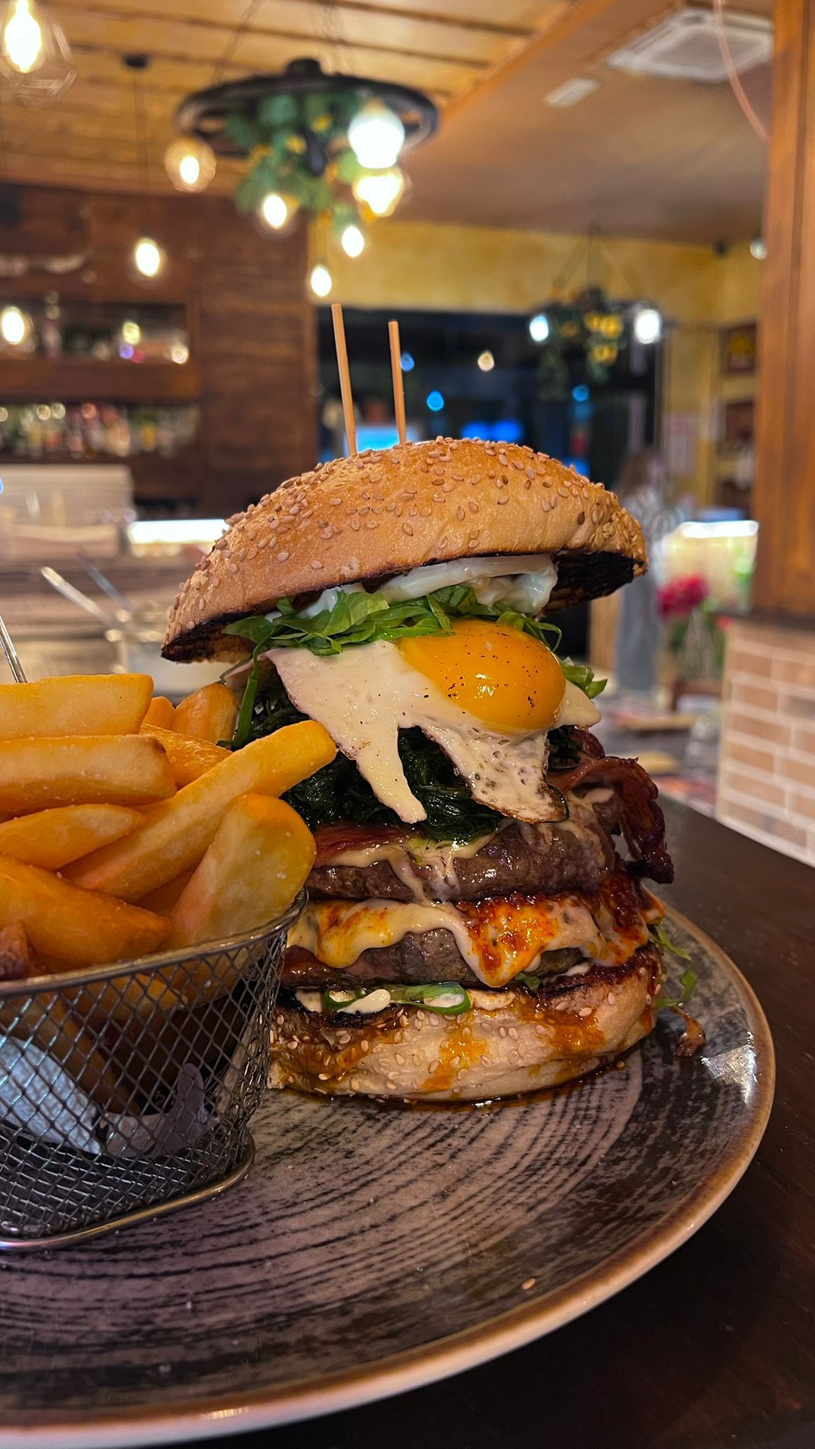 Hamburger doppio con uovo fritto, lattuga e patatine fritte servito su un piatto in un ambiente da ristorante.