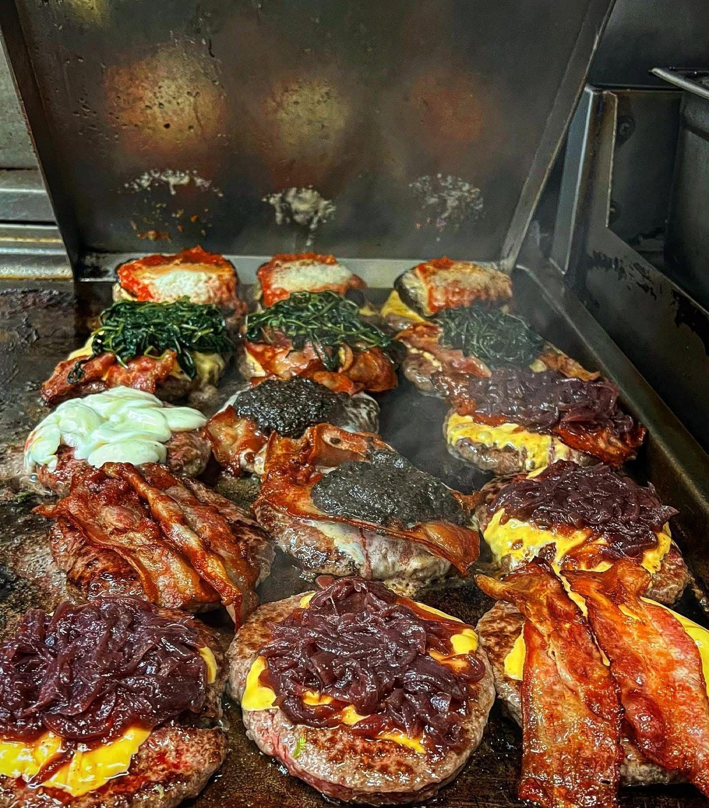 Hamburger alla griglia con vari condimenti, tra cui pancetta e cipolle, cotti nella cucina di un ristorante.