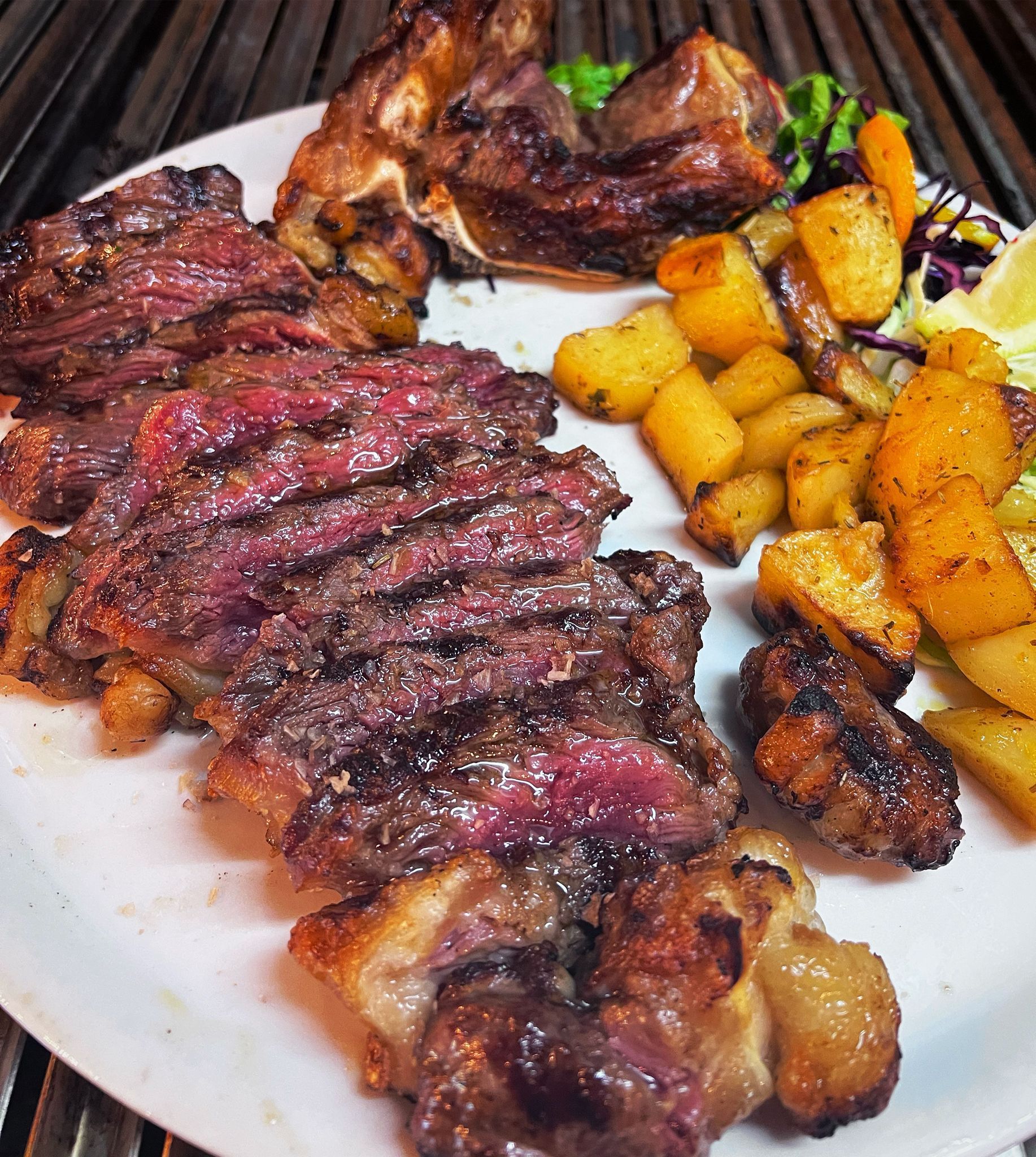 Bistecca alla griglia e costolette di agnello con patate arrosto su un piatto bianco.