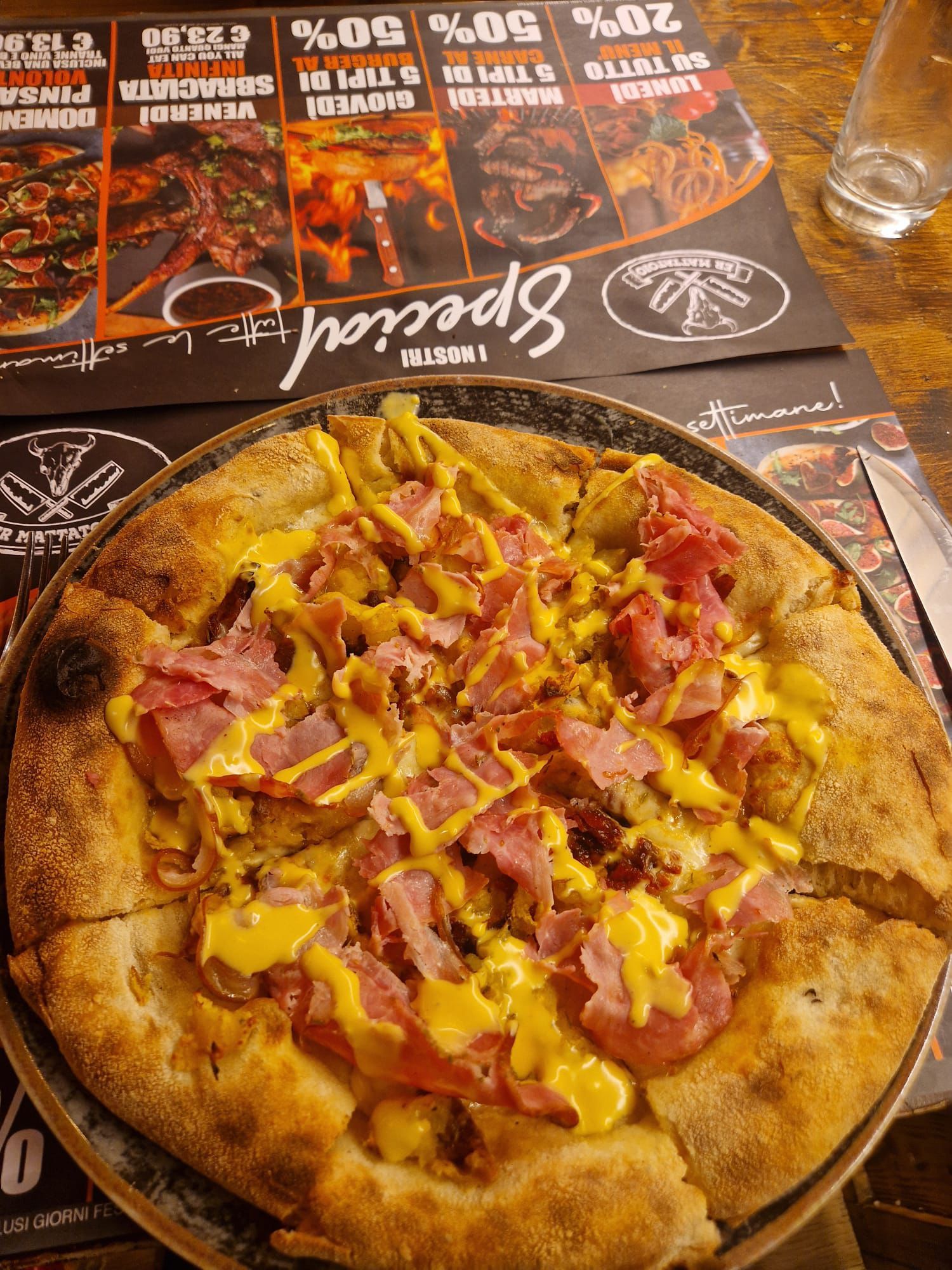 Pizza con prosciutto, senape e crosta dorata, servita sul tavolo di un ristorante.