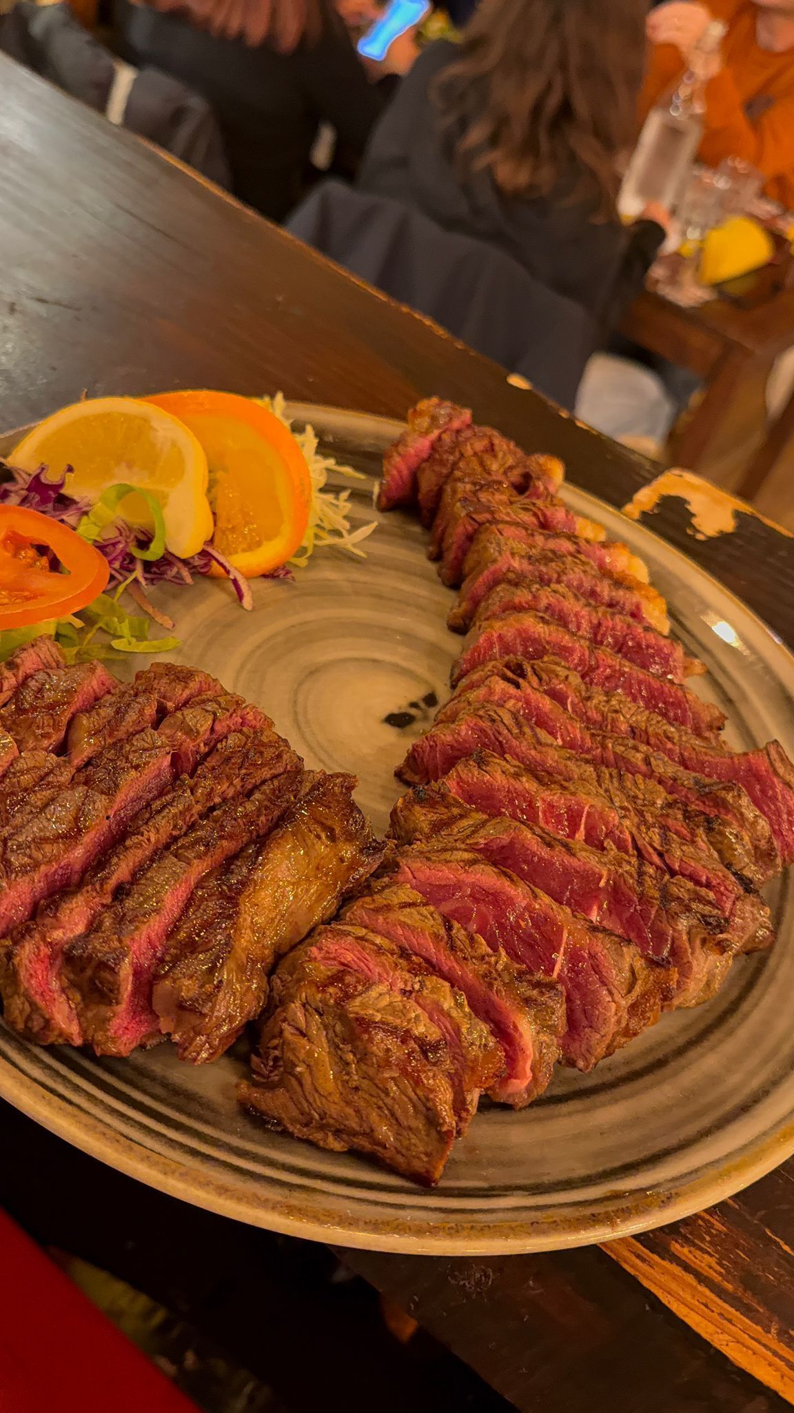 Bistecca tagliata a fette su un piatto con fette d'arancia e guarnizione in un ristorante.