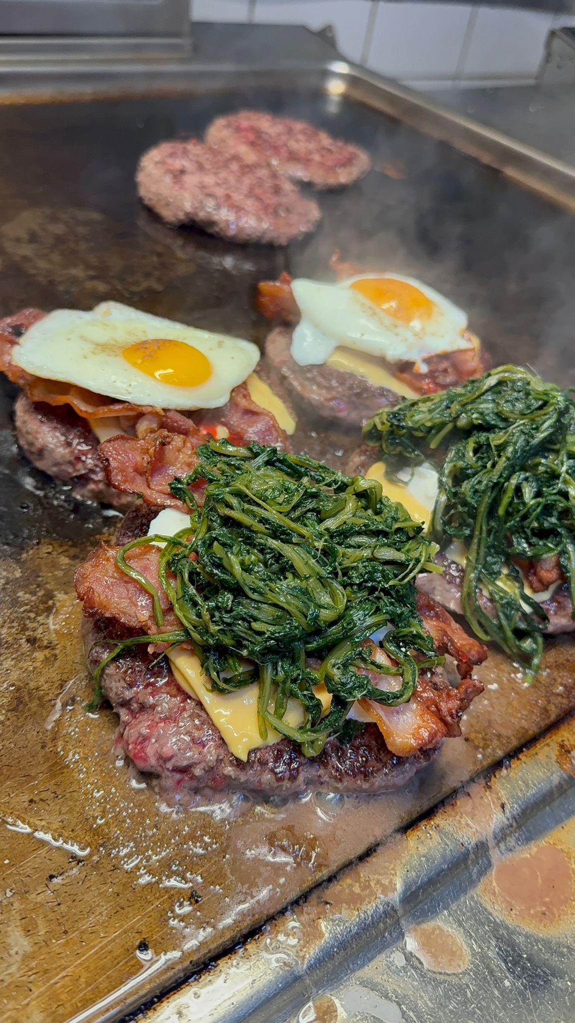 Hamburger con pancetta, uova e spinaci cotti su una piastra.