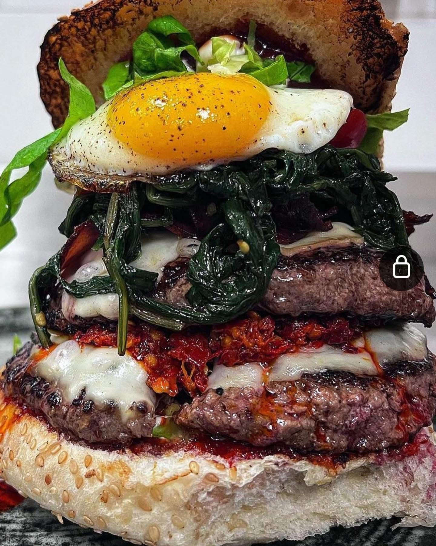 Hamburger doppio con uovo fritto, formaggio, spinaci e salsa di pomodoro su un panino tostato.