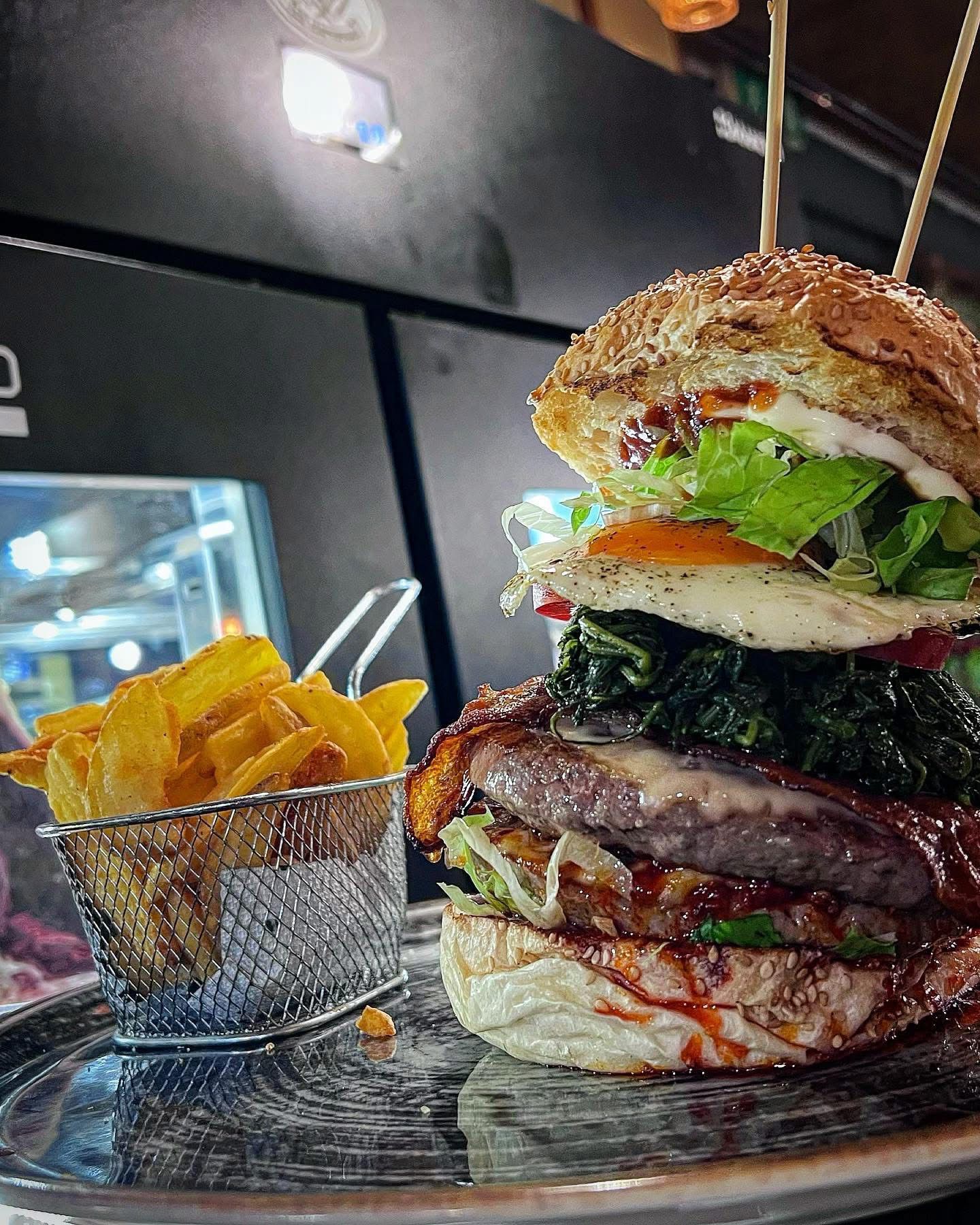 Delizioso hamburger con uovo fritto, verdure e patatine fritte su un piatto d'argento.