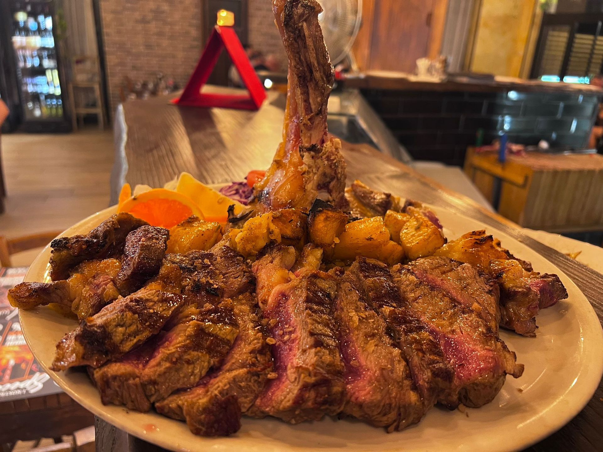 Bistecca tagliata a fette e cotta con verdure arrostite su un piatto bianco in un ristorante scarsamente illuminato.