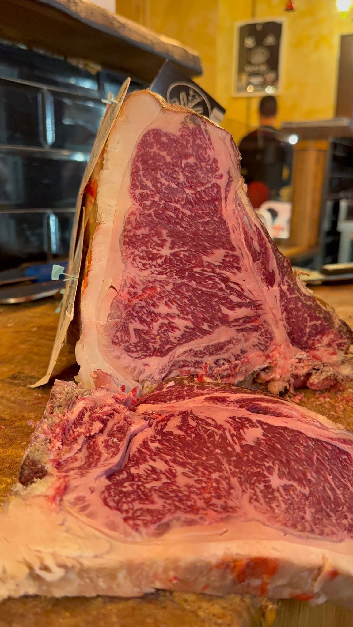 Grande bistecca a T marmorizzata, tagliata a fette e appoggiata su una superficie di legno, con ricche venature di grasso rosso e bianco.