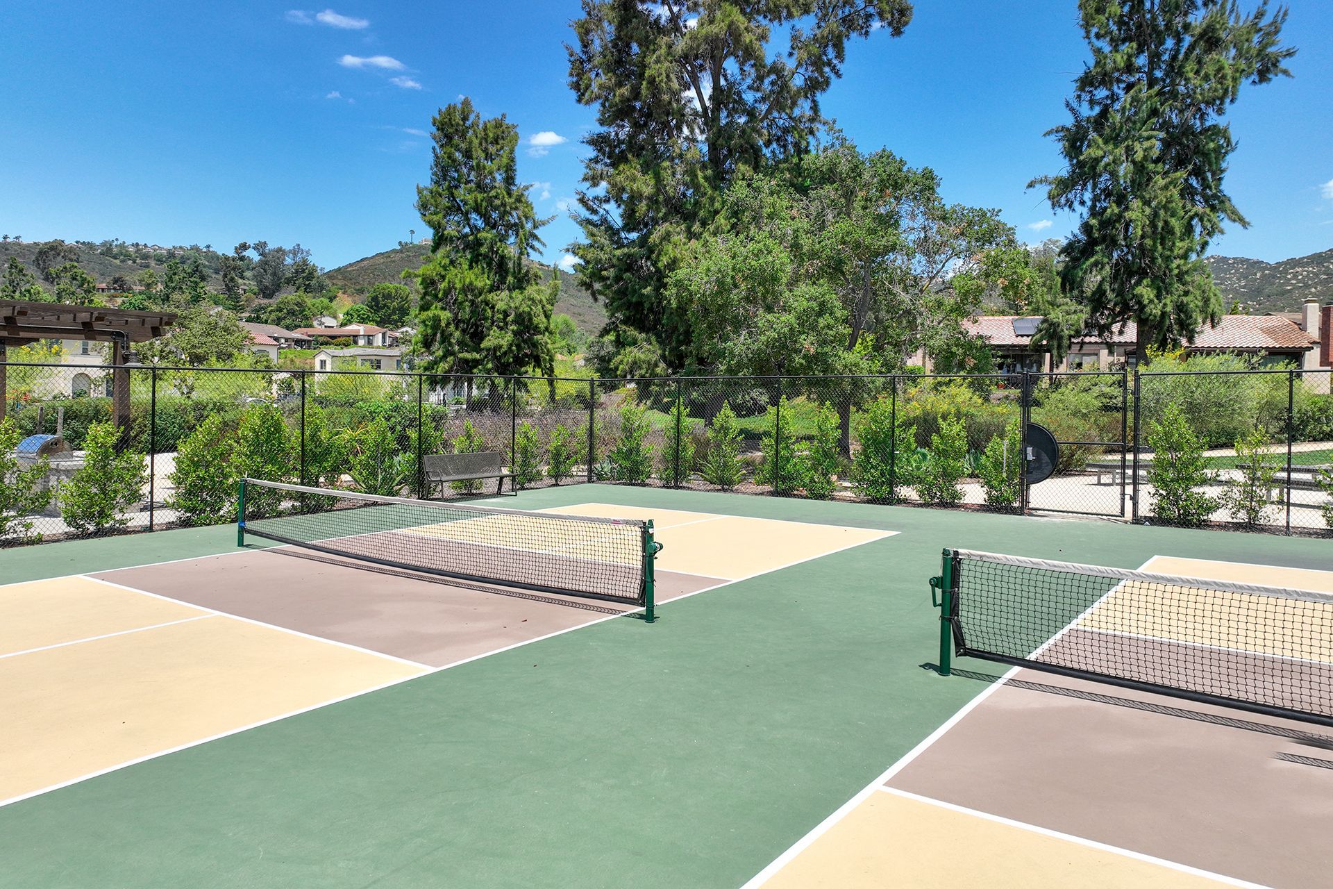Outdoor pickleball courts with nets, surrounded by landscaping, under a sunny blue sky.