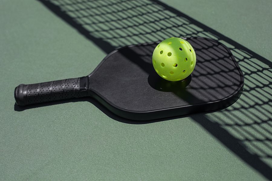 Pickleball paddle and ball on green court, with net shadow.
