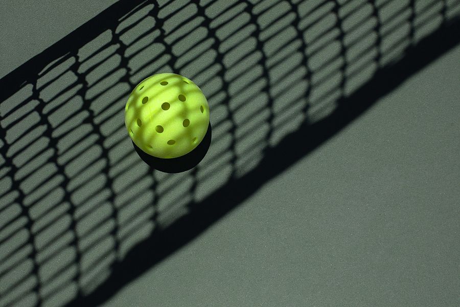 Yellow pickleball on a gray court with a net's shadow.