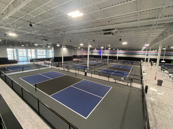 Girl smiles, holding a yellow pickleball and orange paddle on a pickleball court.