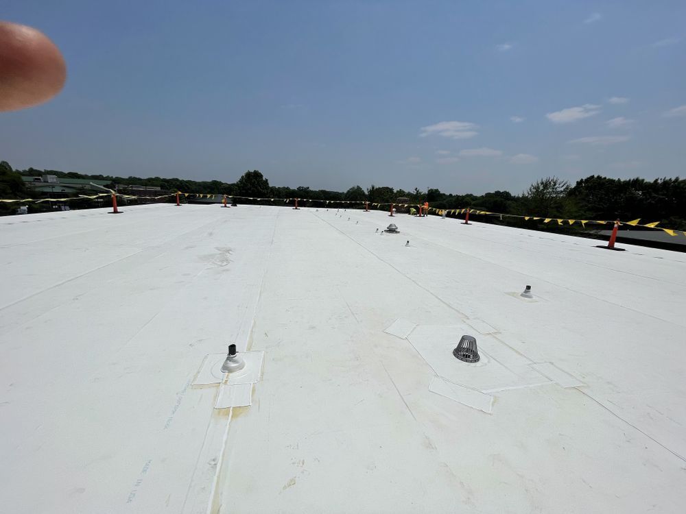 White commercial rooftop under a blue sky, with vents and safety cones.