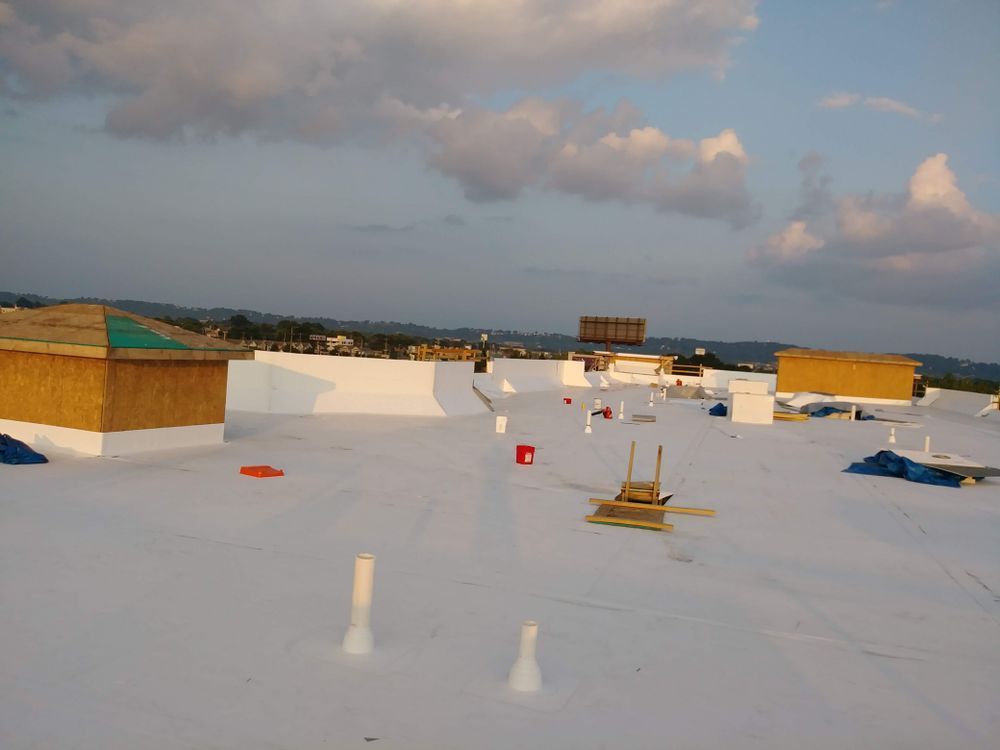 White flat roof with vents and construction materials, against a cloudy sky.