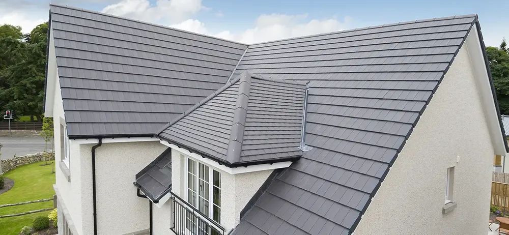 Gray roof tiles on a white house with a dormer and black gutters under a blue sky.