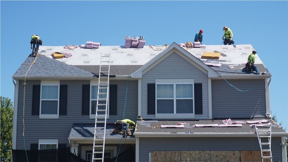 Roofers on a two-story house; installing shingles. 