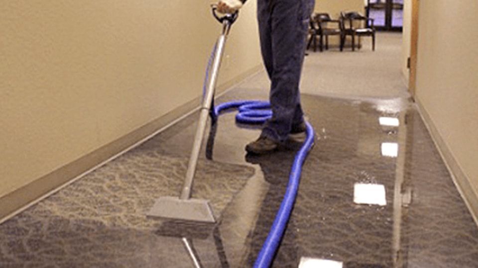 Person cleaning a dark, reflective floor with a machine in a hallway.