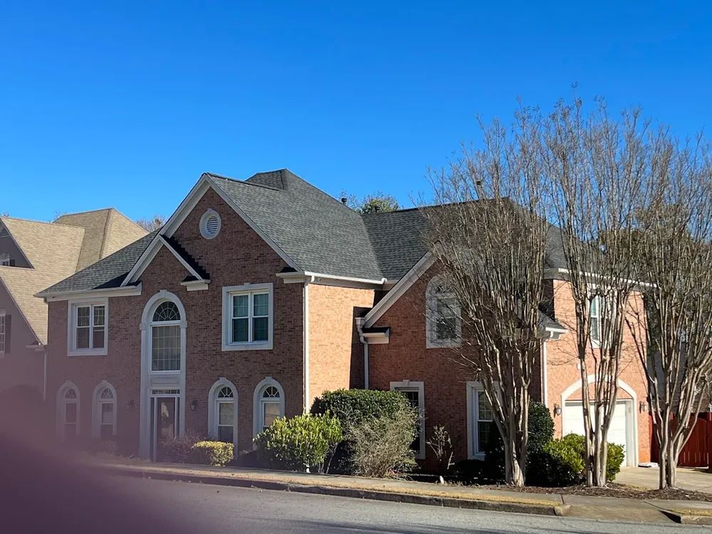Two-story brick house with dark roof and two-car garage; bare trees in front.