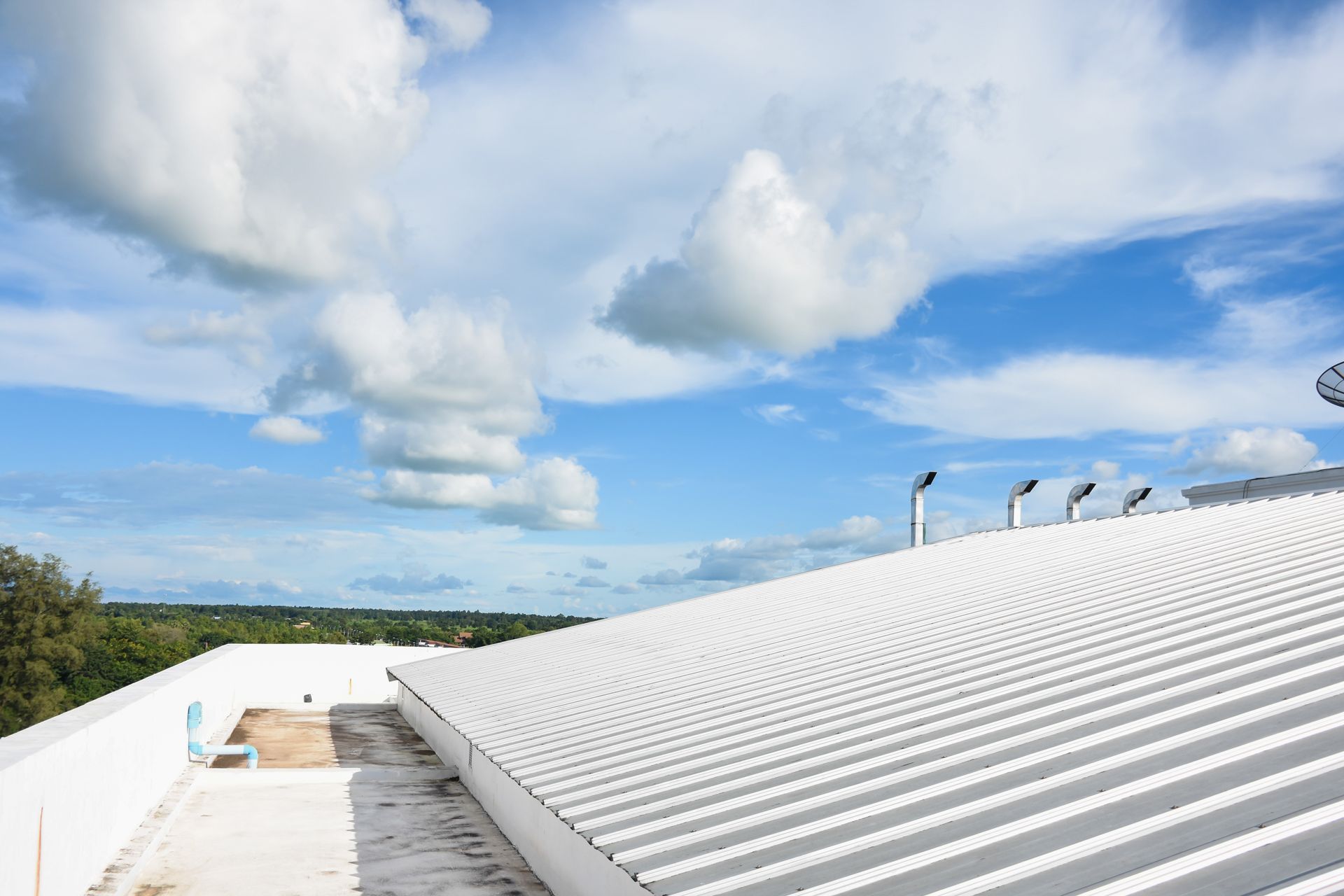 Person in hard hat on a white commercial rooftop, sunny day, blue sky.