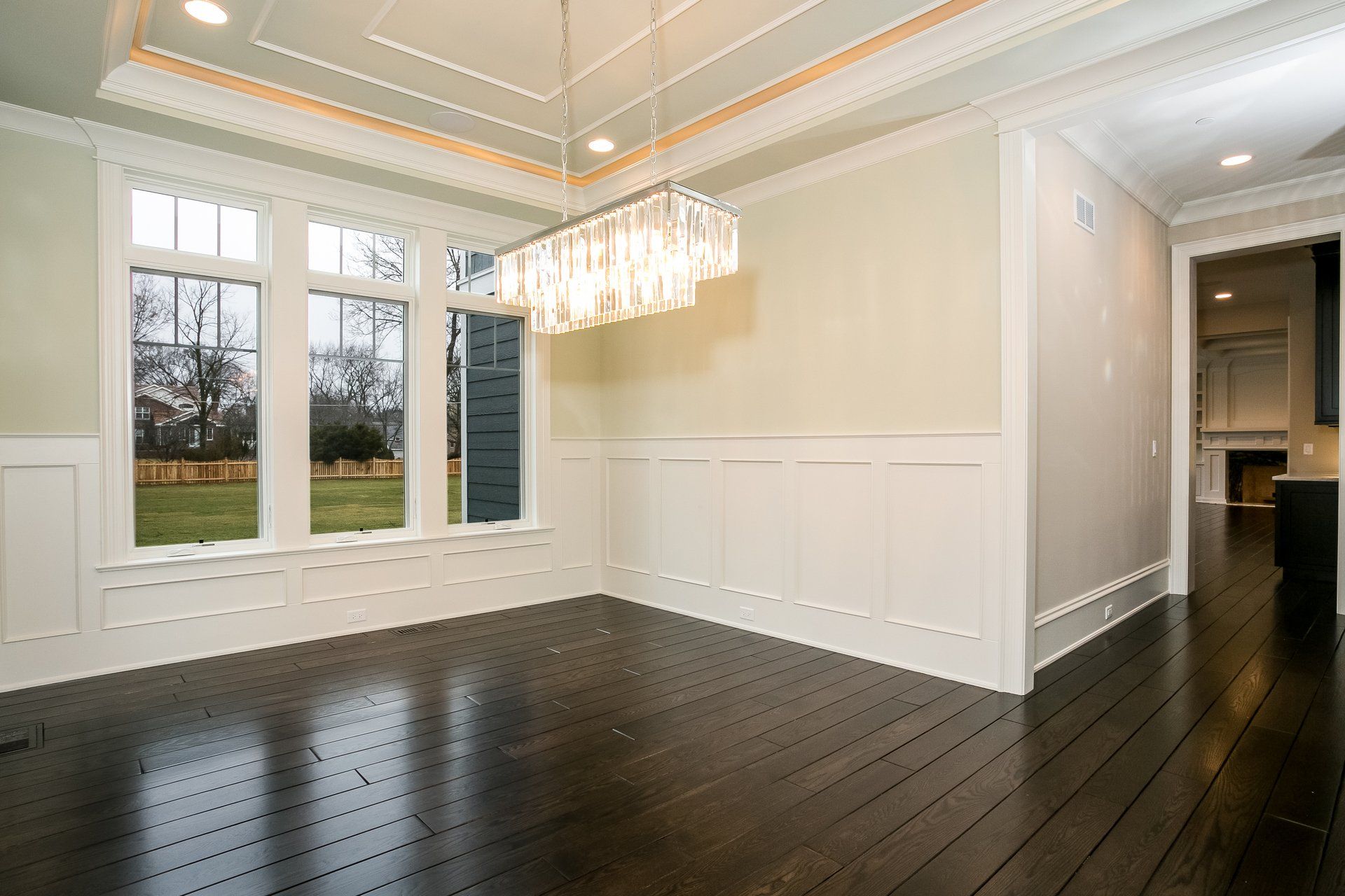 An empty dining room with hardwood floors and a chandelier hanging from the ceiling.