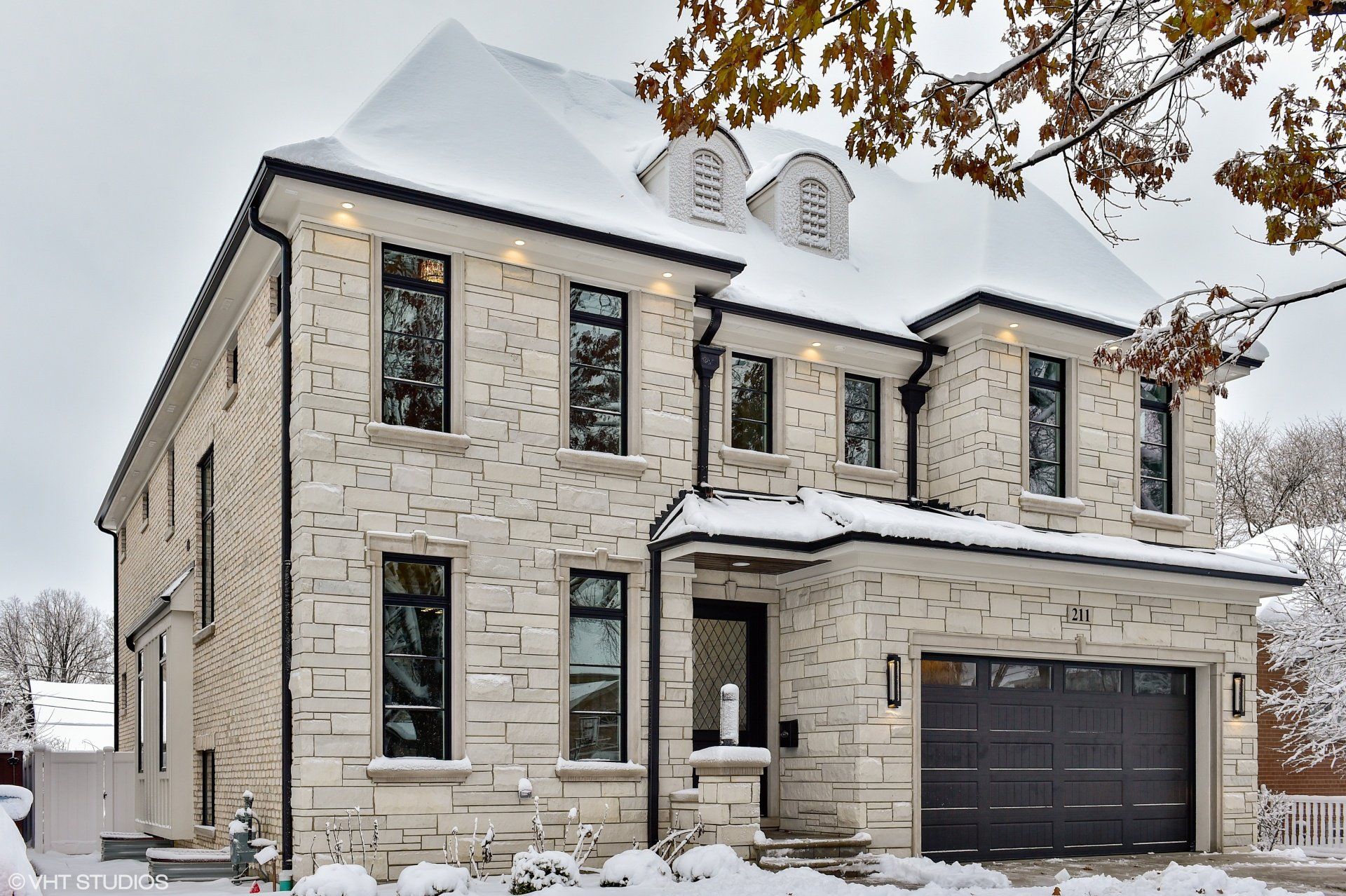 A large white brick house with a black garage door is covered in snow.