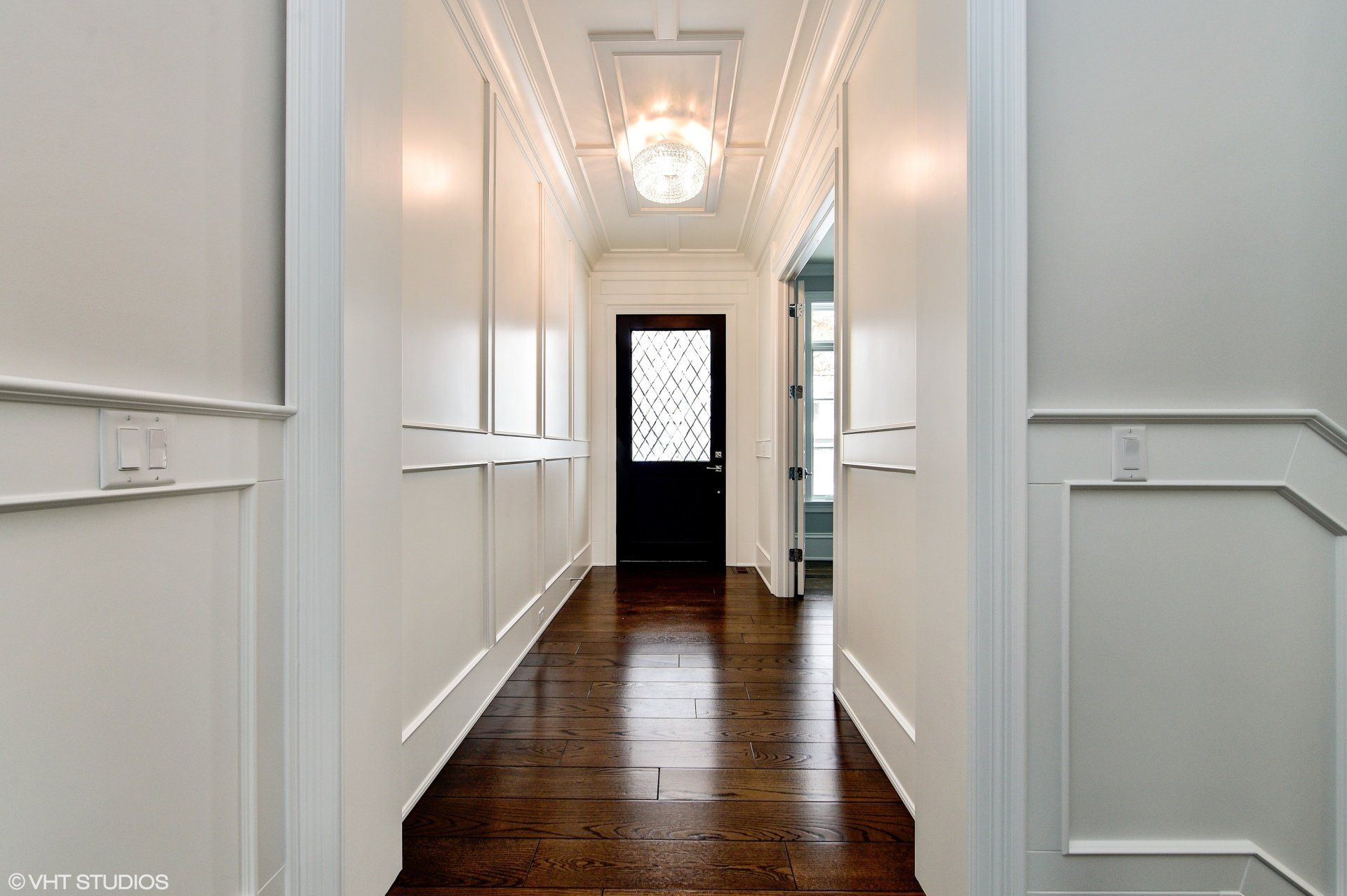 A long hallway with a black door and a chandelier.