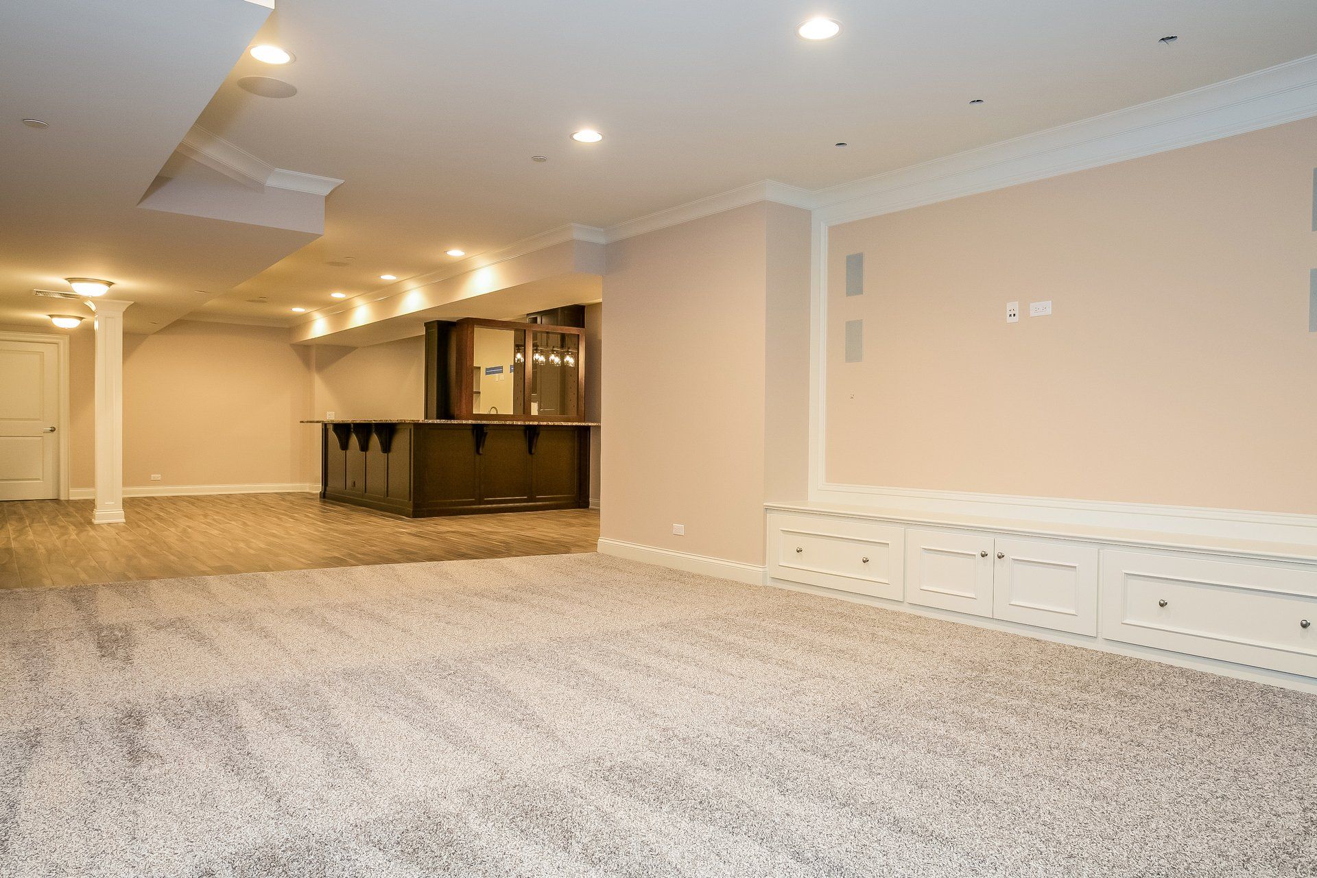An empty basement with a carpeted floor and a bar.
