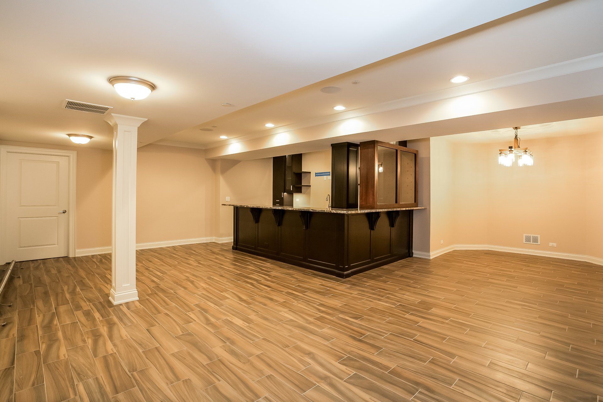 An empty basement with hardwood floors and a bar.