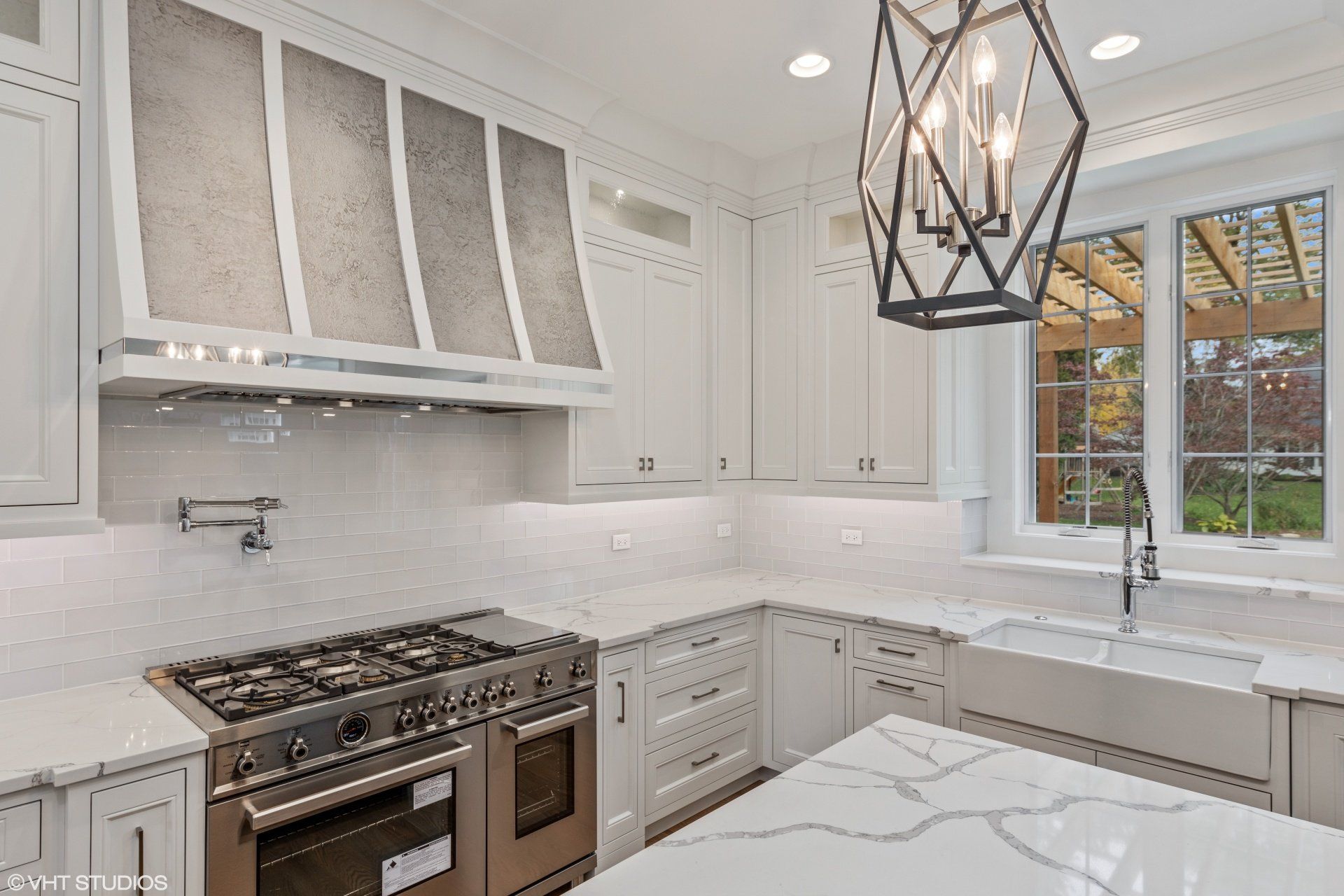 A kitchen with white cabinets , a stove , a sink , and a chandelier.