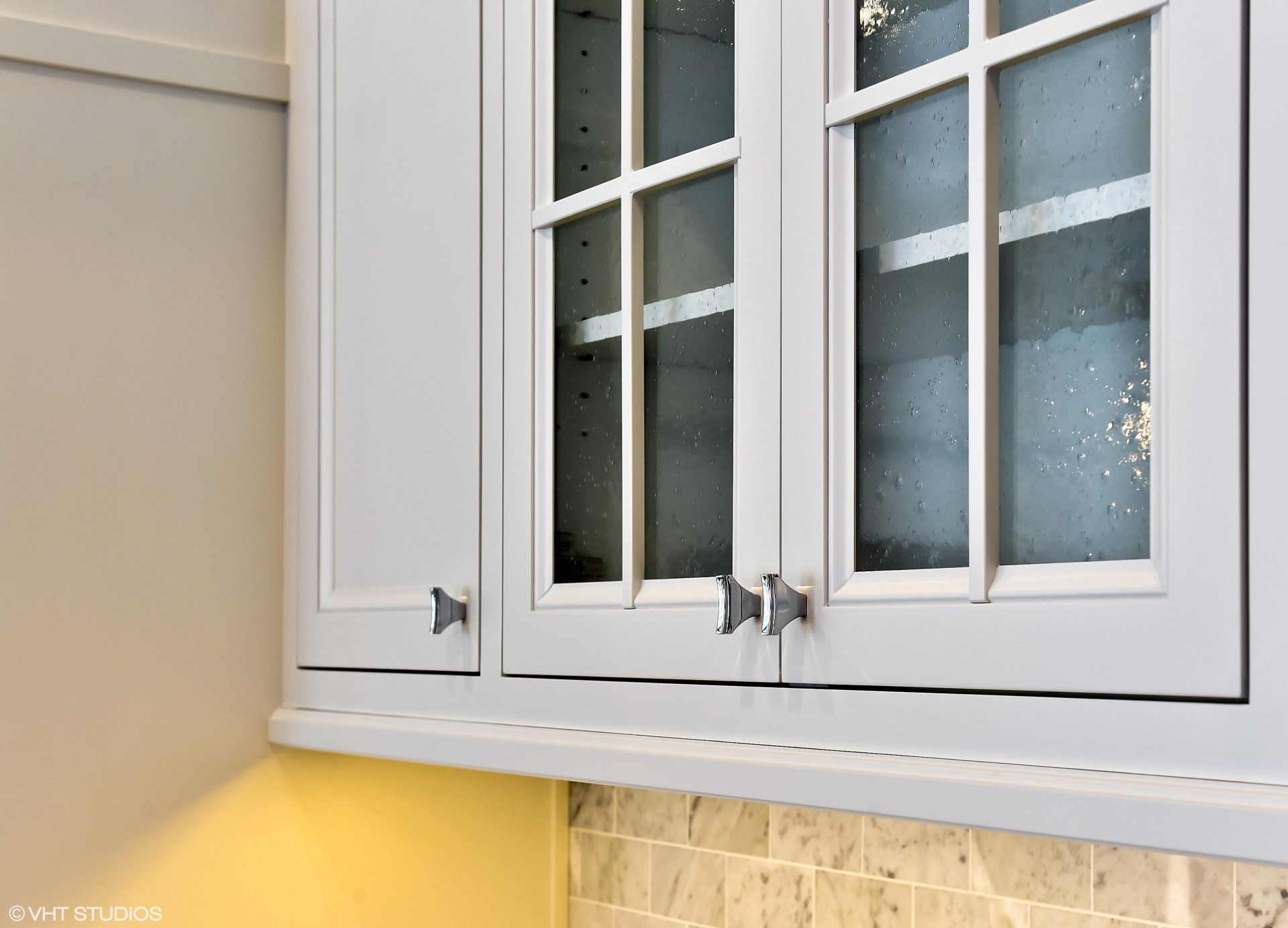 A kitchen with white cabinets and glass doors.
