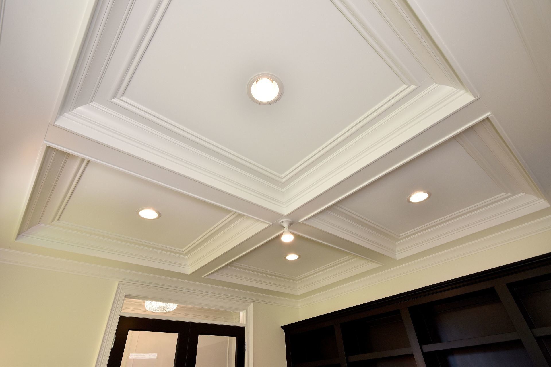 A living room with a coffered ceiling and a black door.