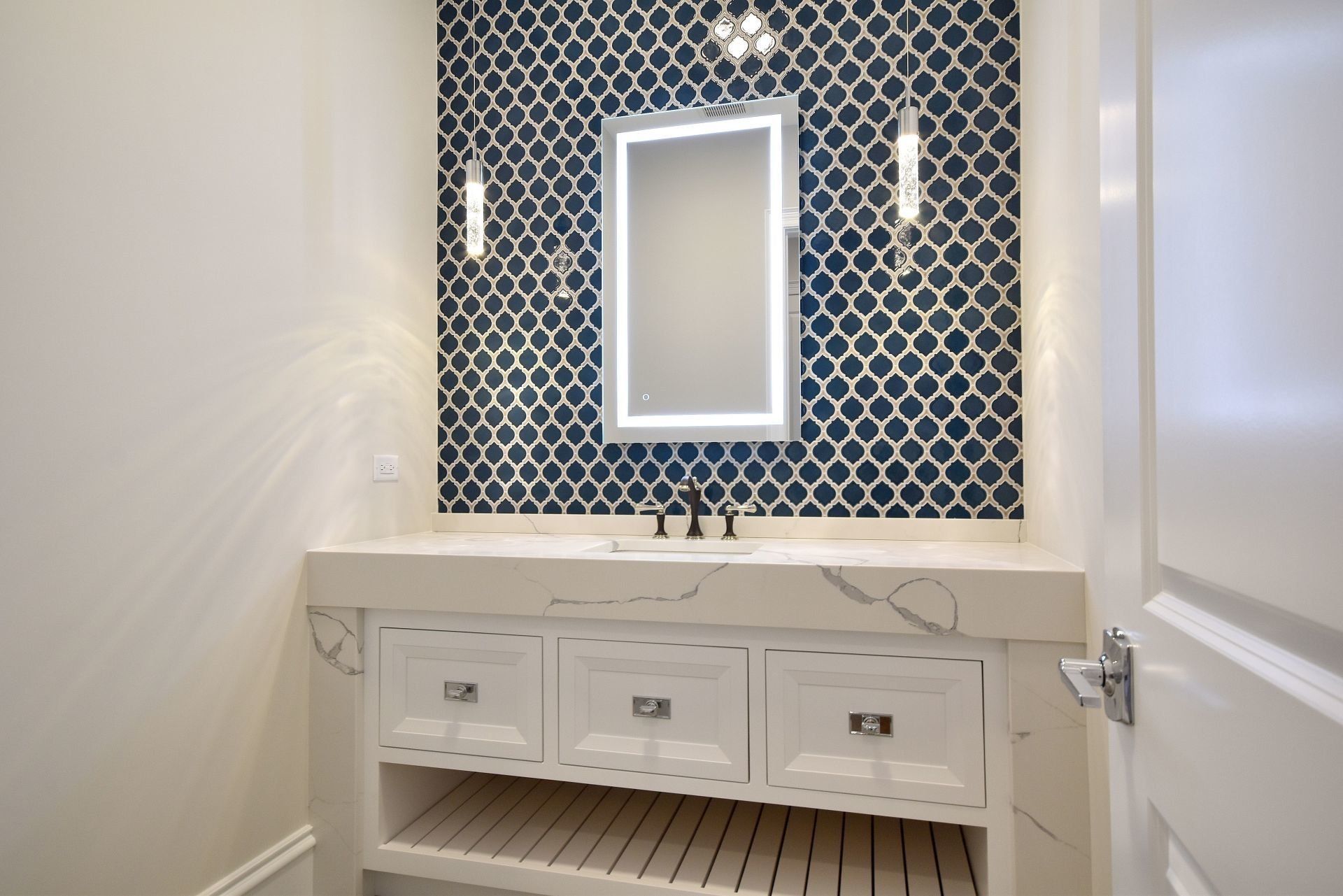 A bathroom with a sink , mirror and blue tiles.