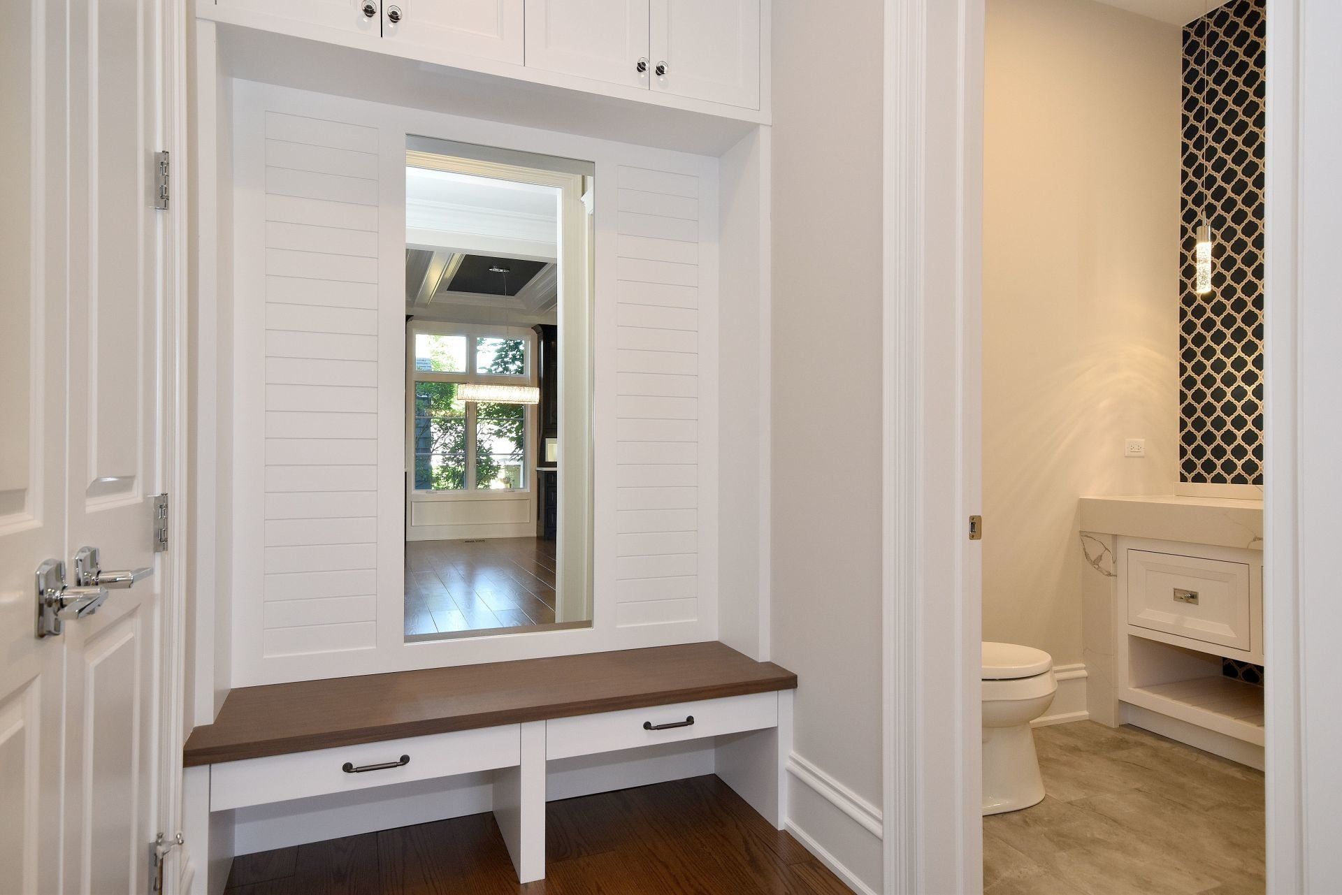 A hallway with a bench and a mirror leading to a bathroom.