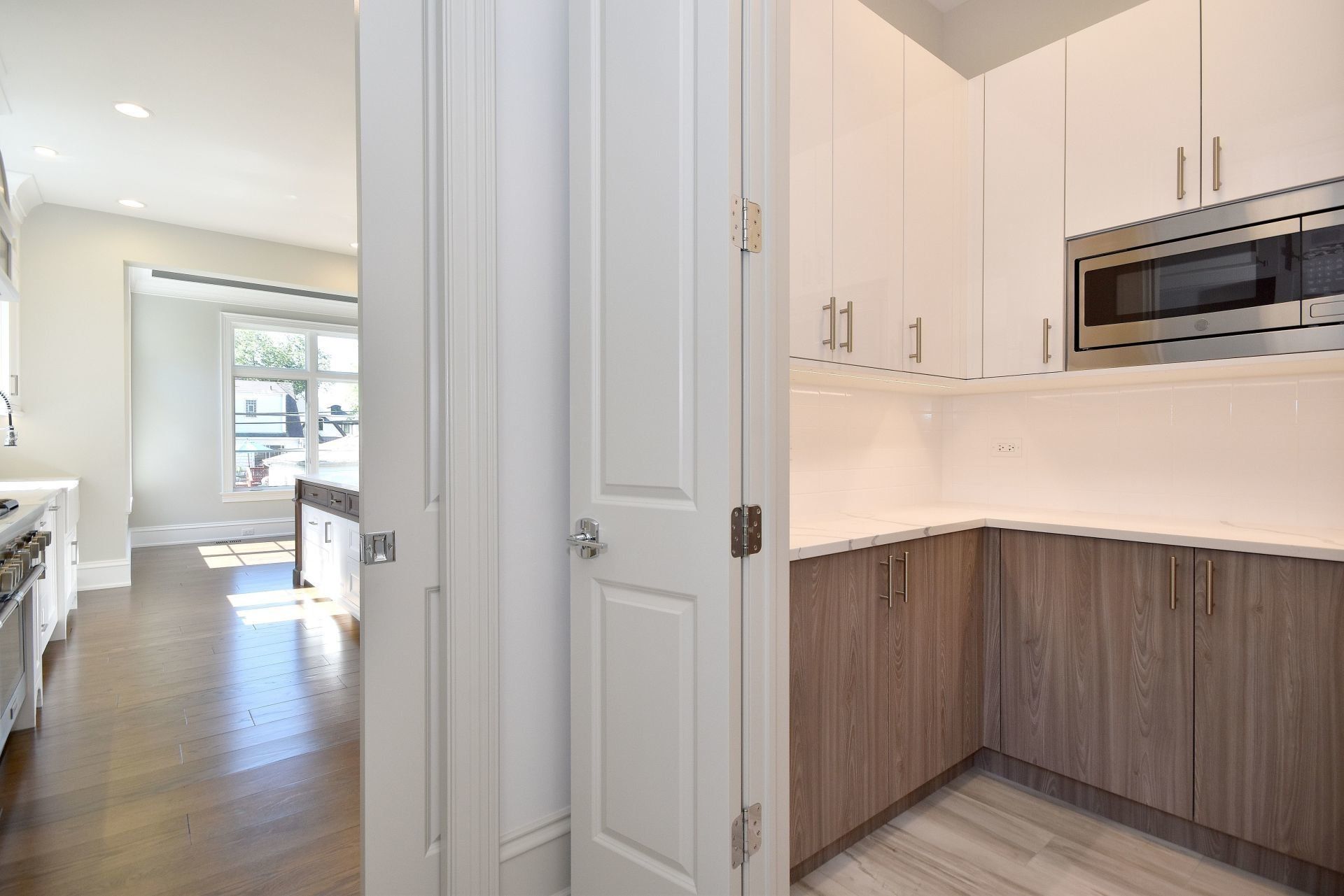 A kitchen with white cabinets and wooden cabinets and a microwave.