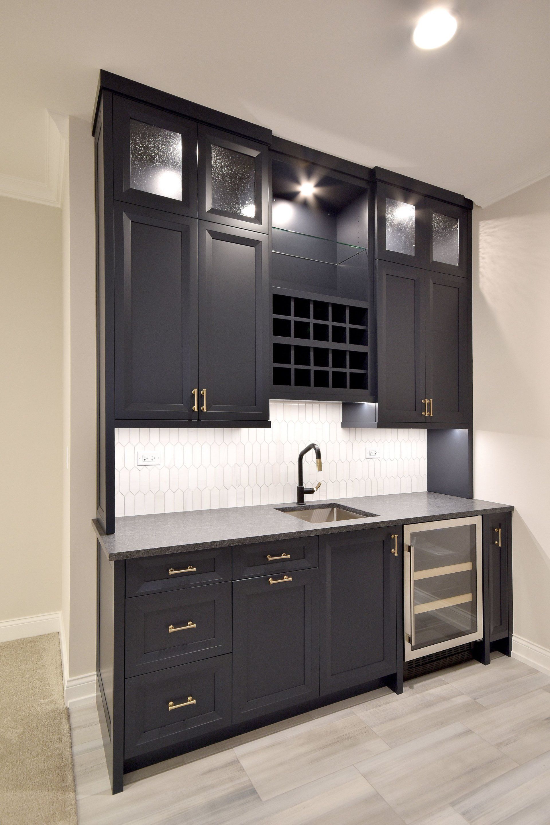 A kitchen with black cabinets , a sink , and a wine cooler.