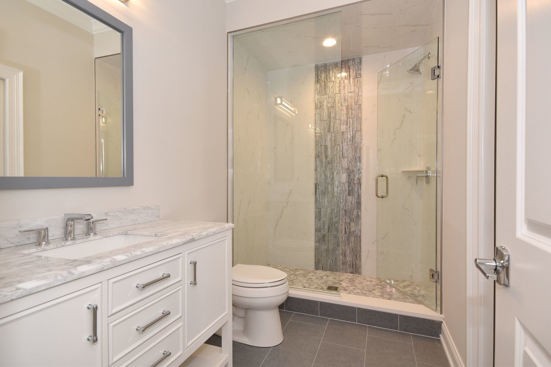 A bathroom with a toilet , sink , mirror and walk in shower.