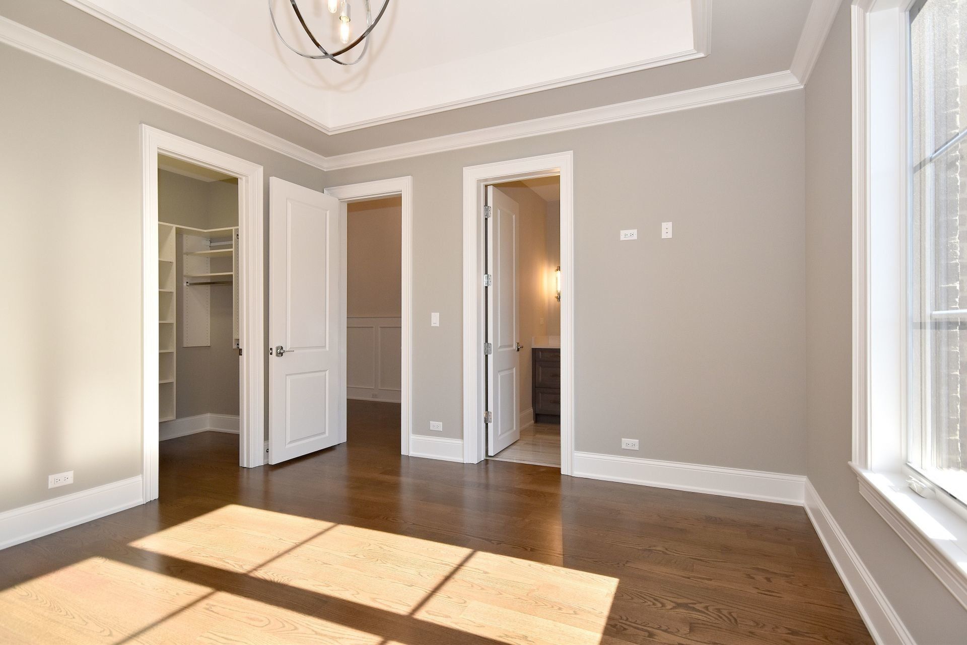 An empty room with hardwood floors , gray walls and white trim.