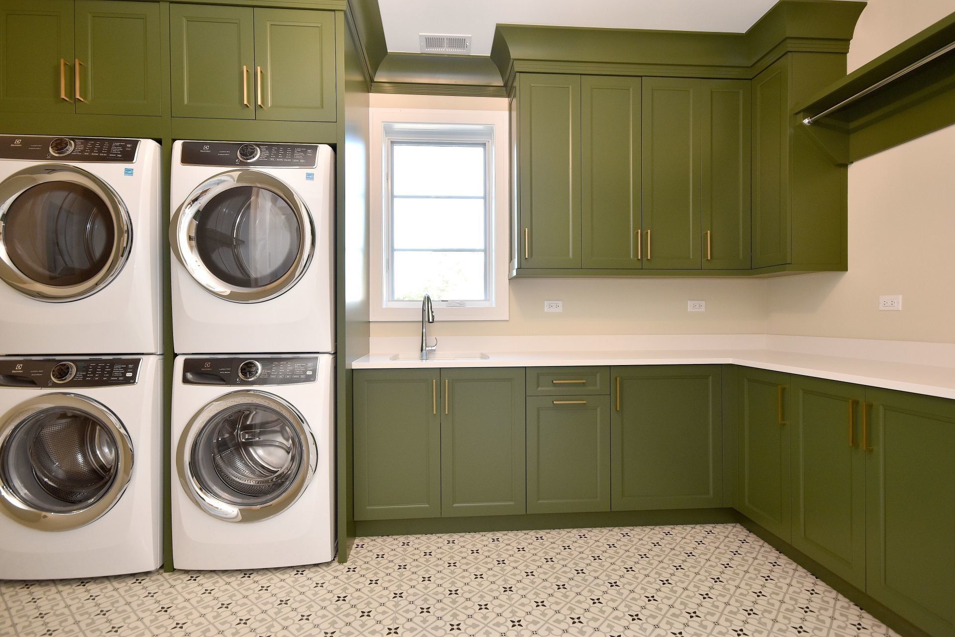 A laundry room with green cabinets and two washers and dryers stacked on top of each other.