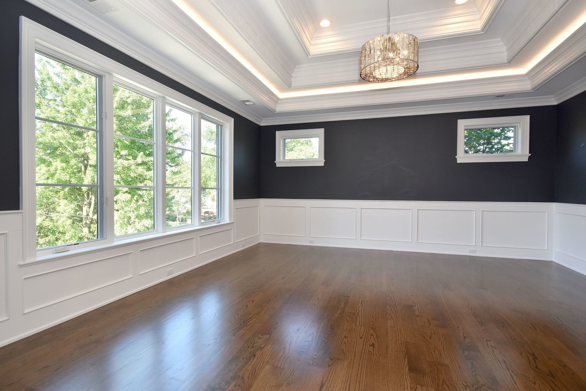 An empty room with hardwood floors and a chandelier hanging from the ceiling.