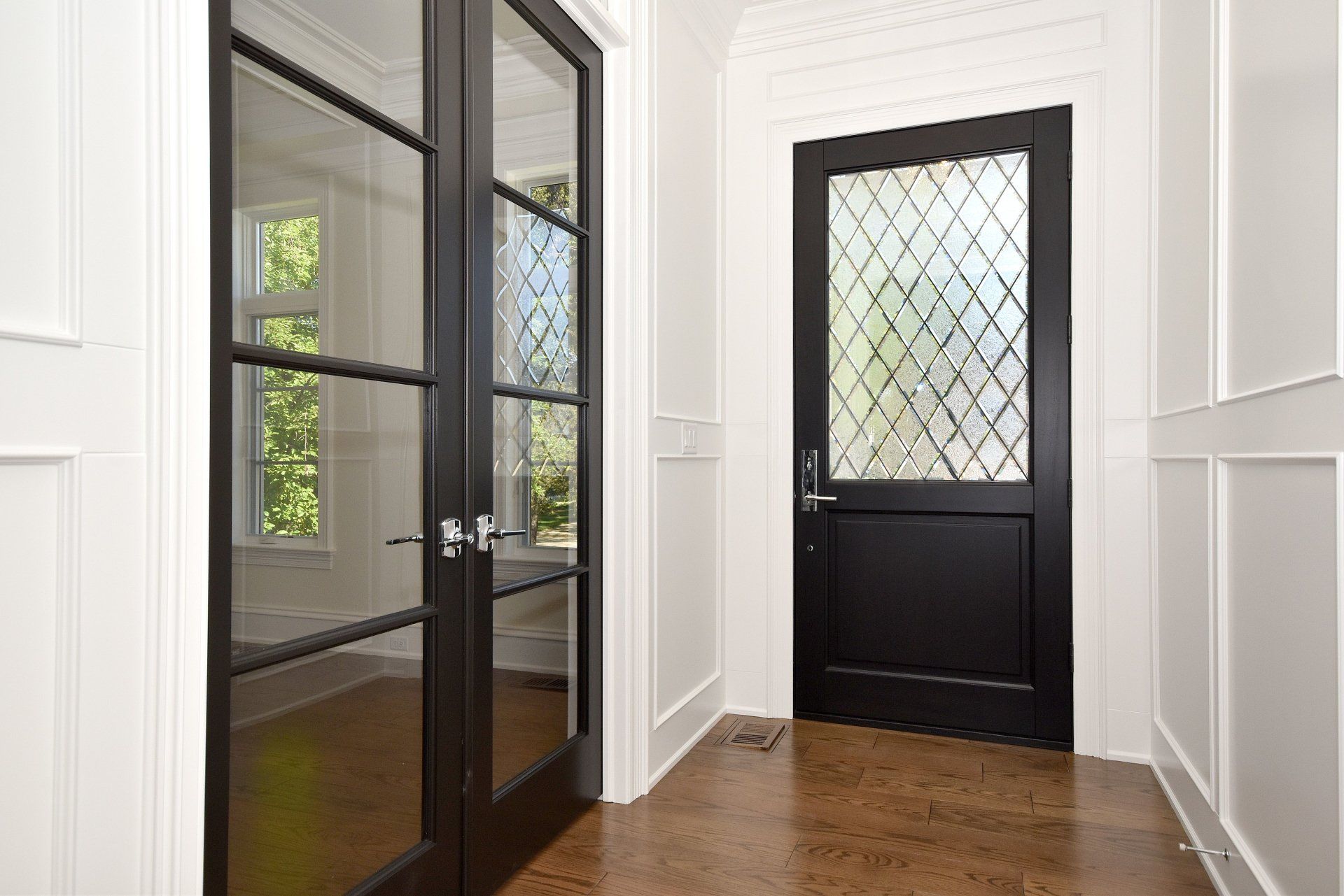 A hallway with a black door and a glass door.