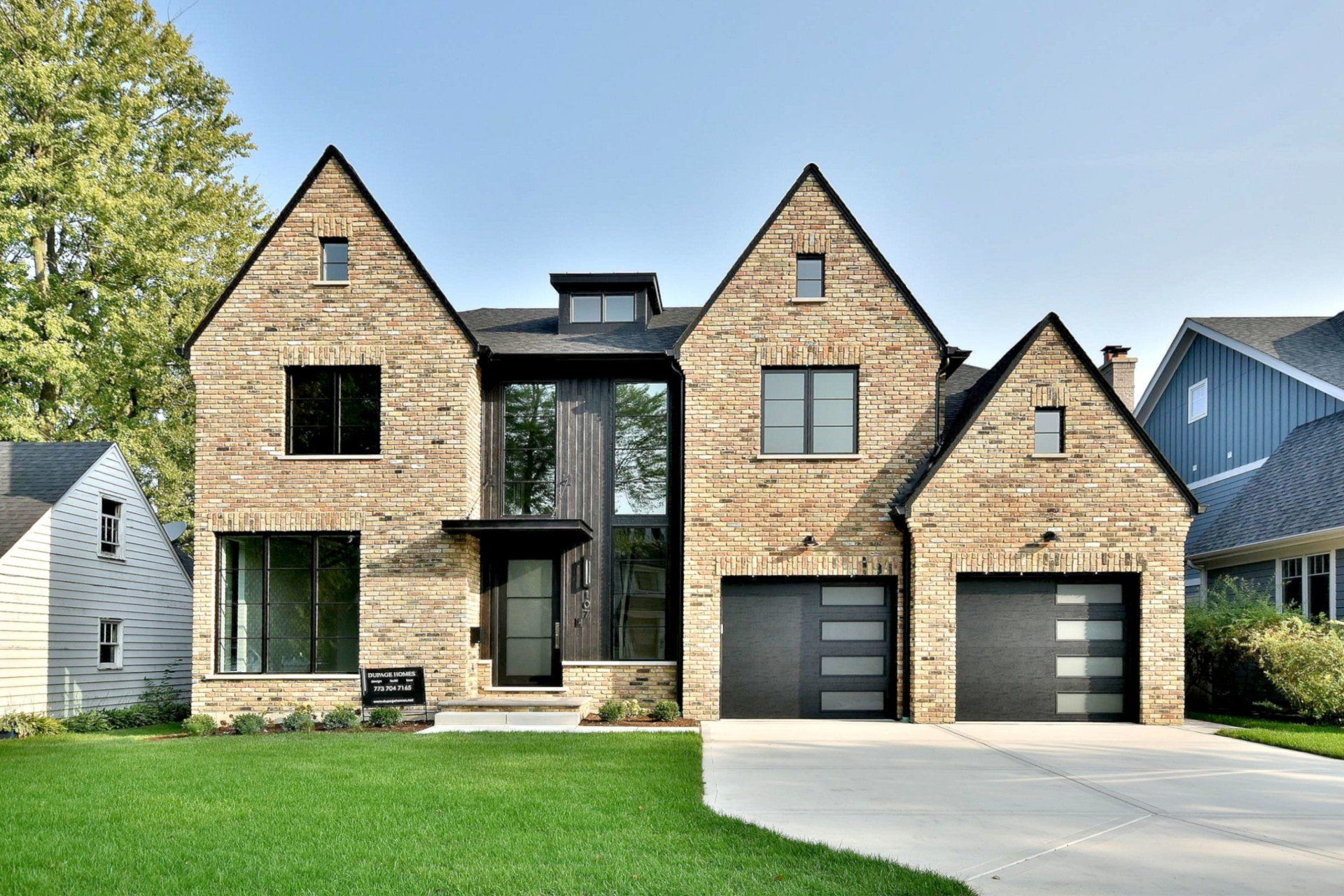 A large brick house with two garages is sitting on top of a lush green lawn.