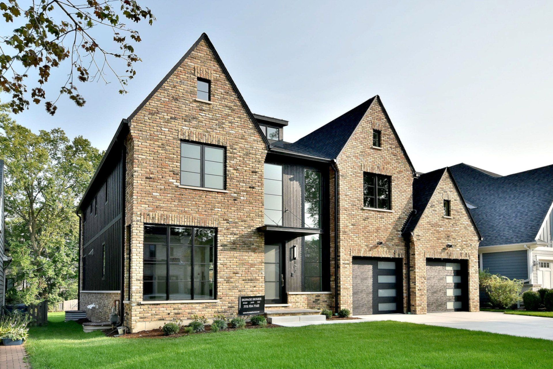 A large brick house with a black roof is sitting on top of a lush green lawn.