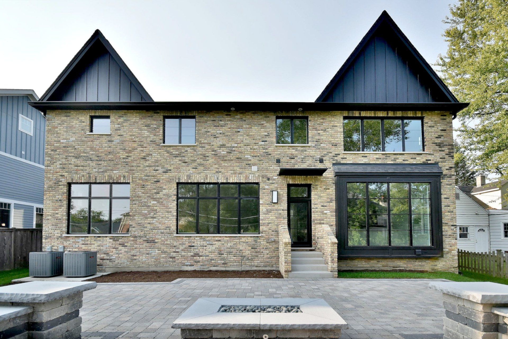 A large brick house with a black roof has a fire pit in front of it.