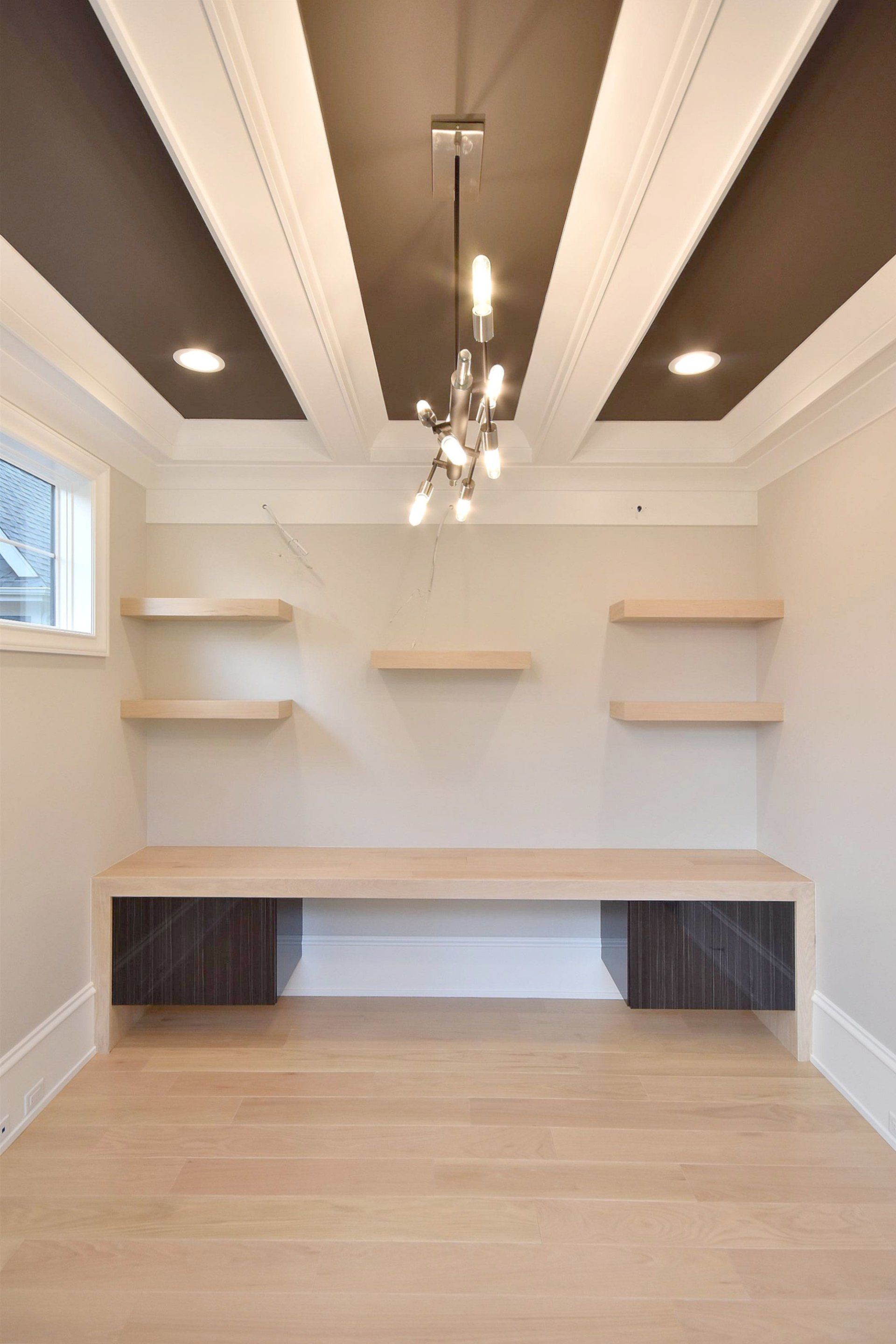 An empty room with a desk and shelves and a chandelier.