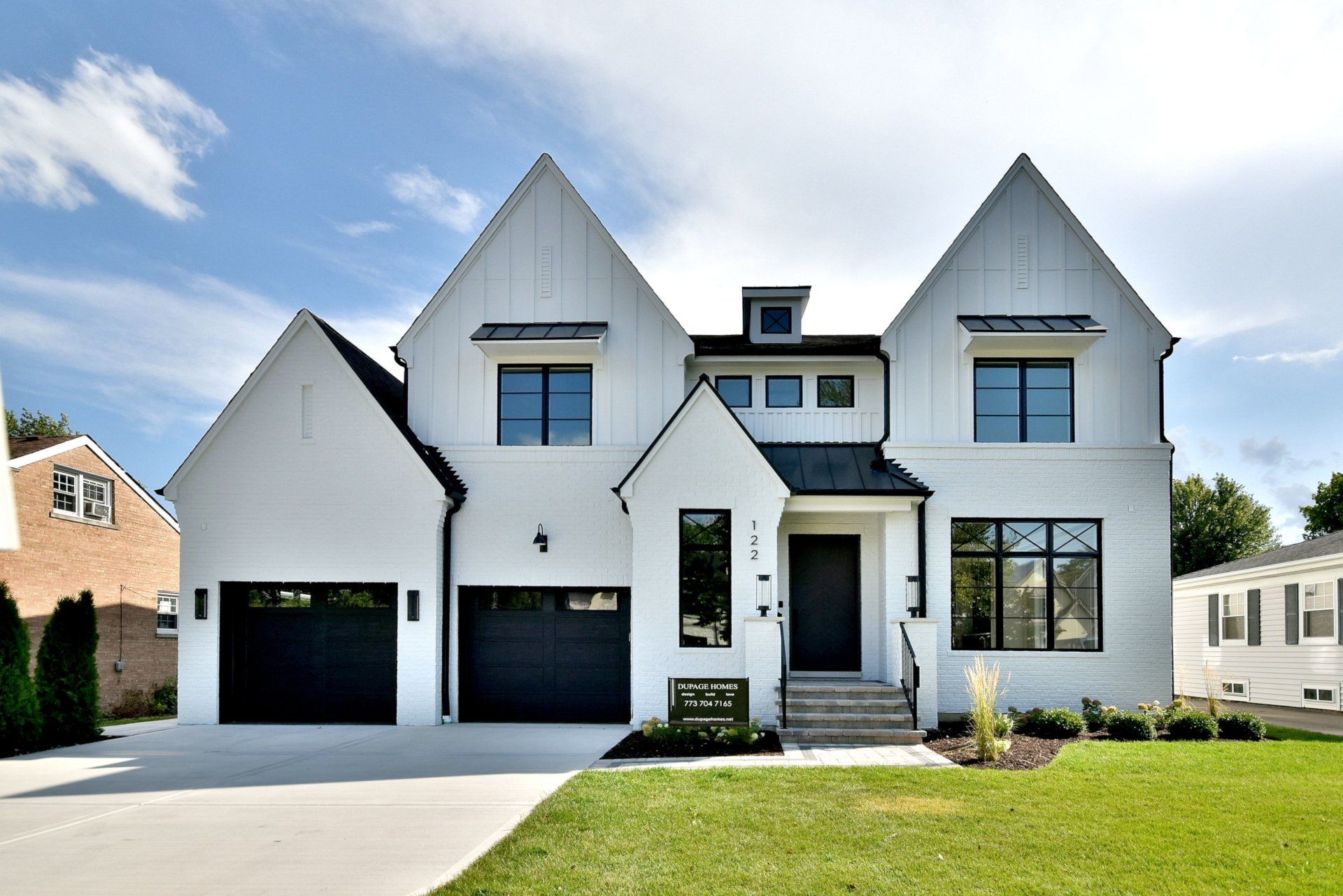 A large white house with a black roof and black garage doors.