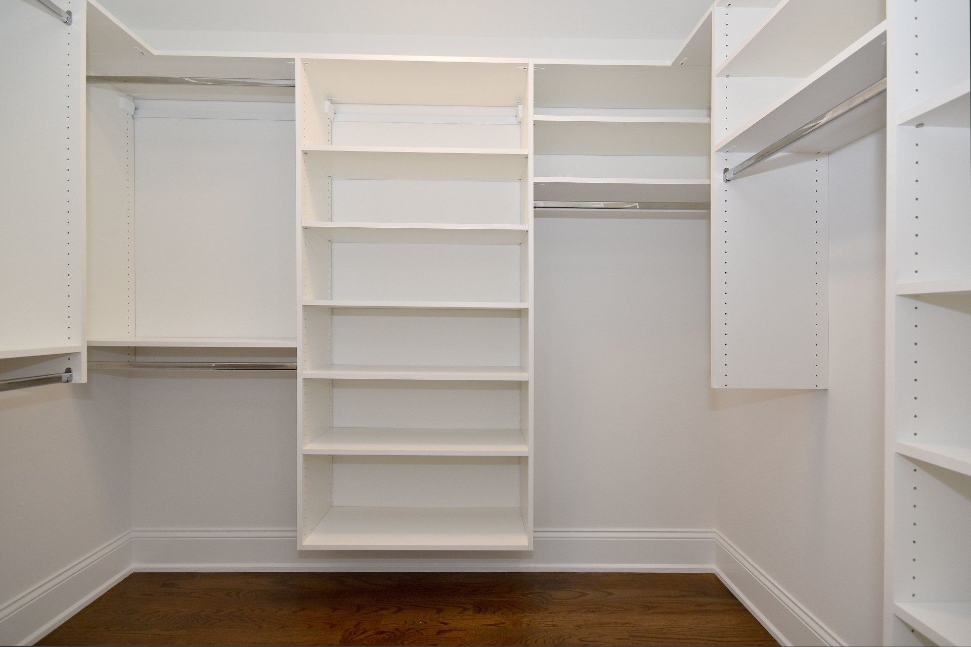 An empty walk in closet with white shelves and wooden floors.